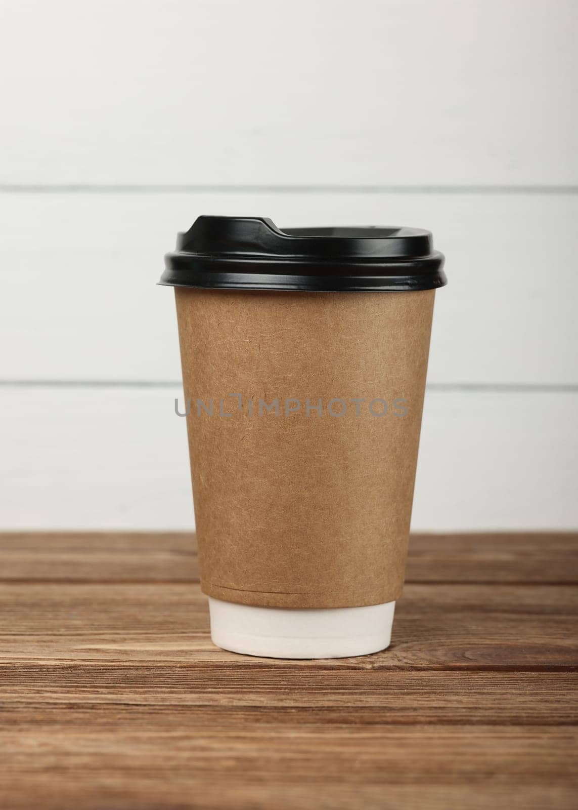 Close up brown paper coffee cup over white wooden painted wall at coffee shop retail display