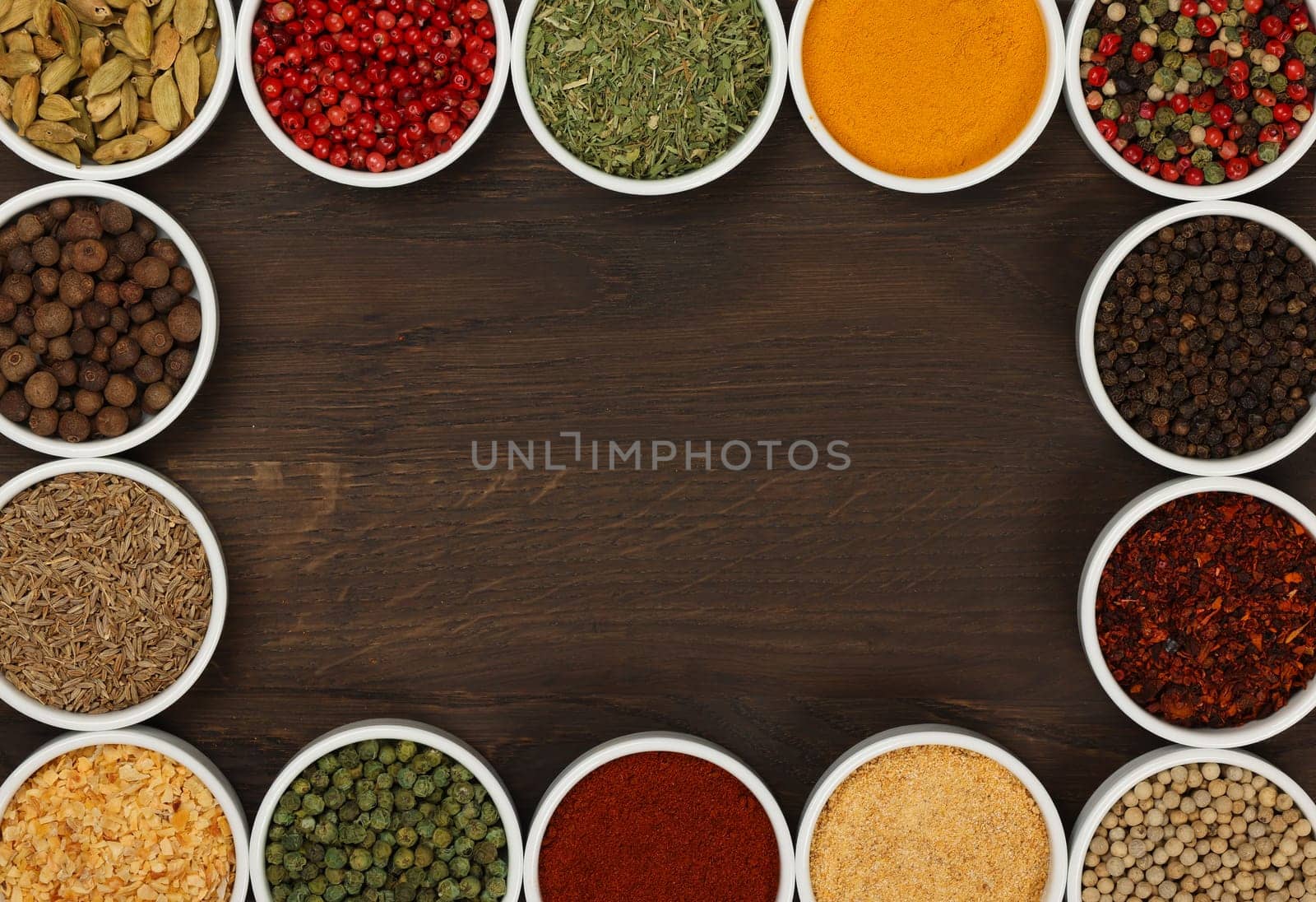 Frame of assorted spices in white ceramic bowls over dark wooden table background with copy space, elevated top view, directly above