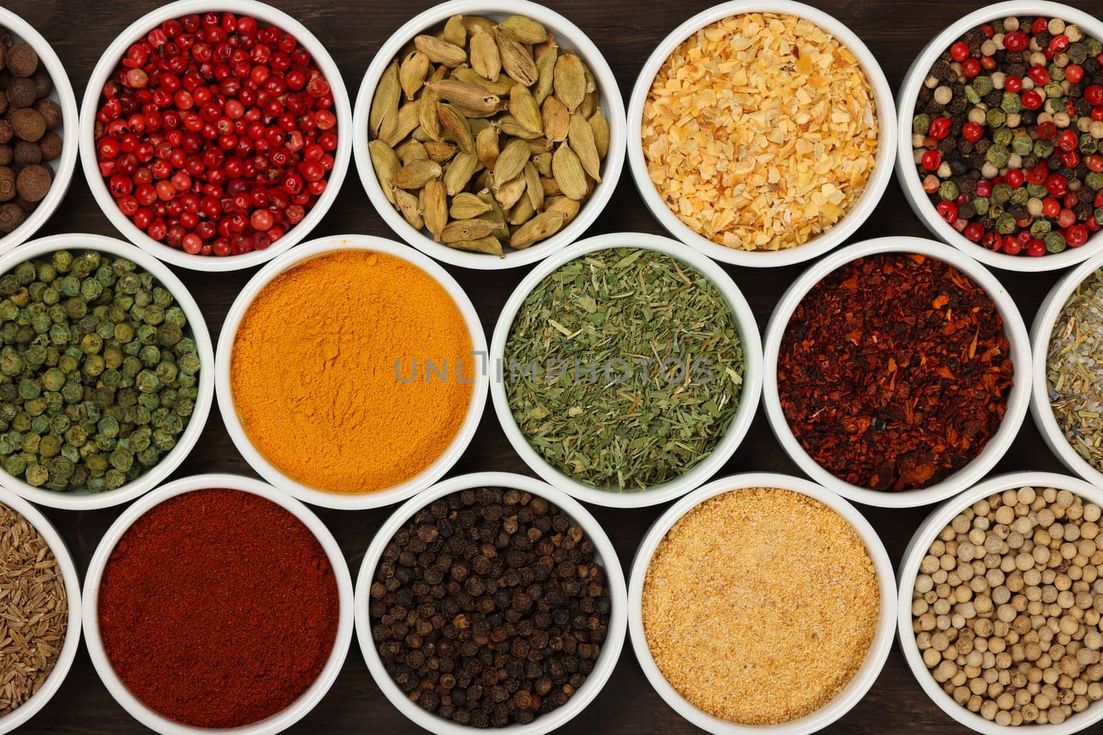 Many white ceramic bowls of assorted spices over dark wooden table background, elevated top view, directly above