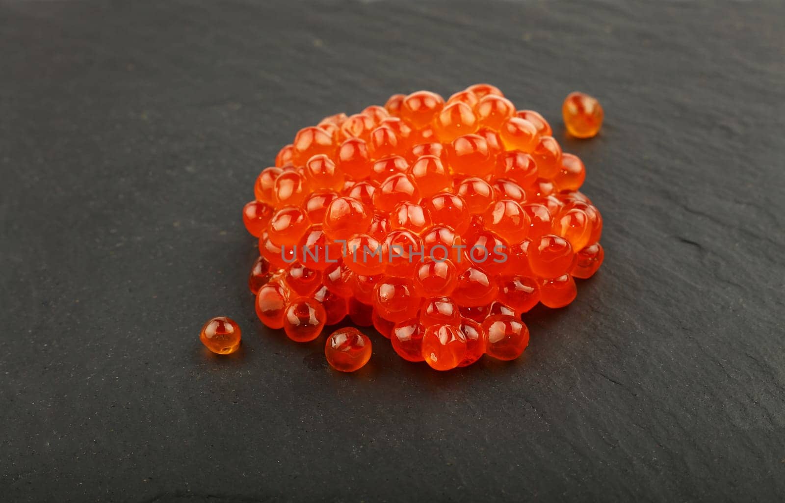 Close up one heap portion of salmon fish red caviar on background of black slate kitchen board, high angle view