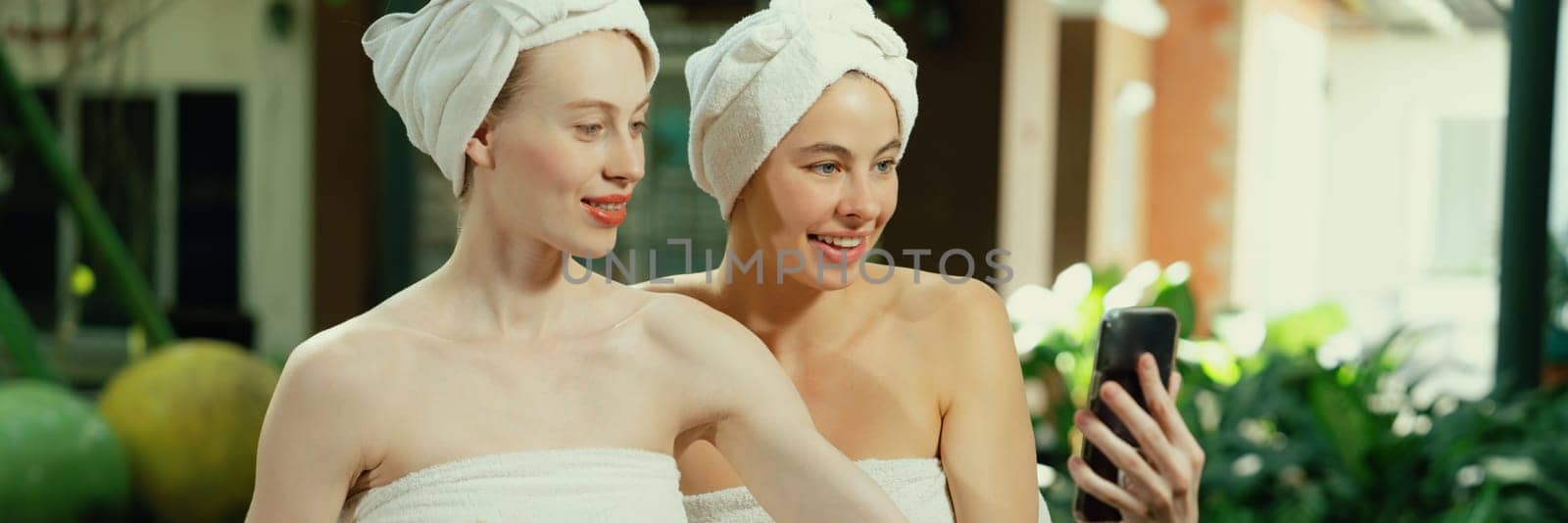 Couple of young beautiful women with beautiful skin in white towel taking a photo together at outdoor surrounded by peaceful natural environment. Beauty and healthy spa concept. Tranquility.