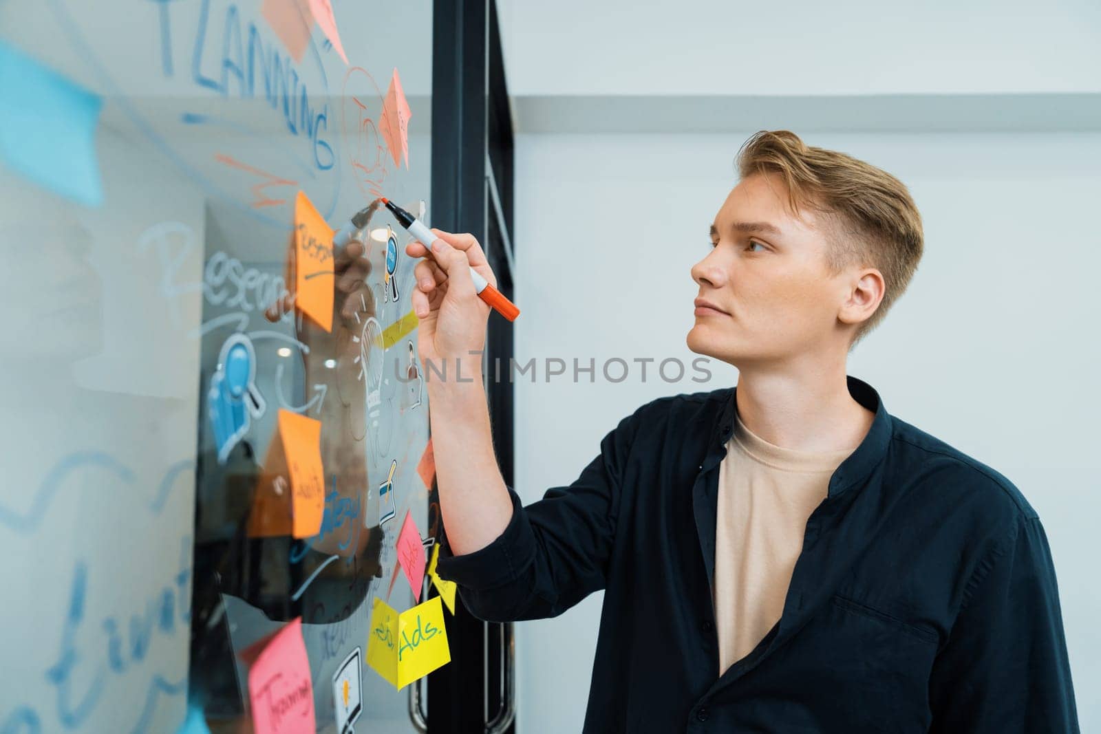 Professional caucasian male leader writing and sharing marketing idea by using mind map and sticky notes on glass board at modern meeting room. Creative business and planing concept. Immaculate.