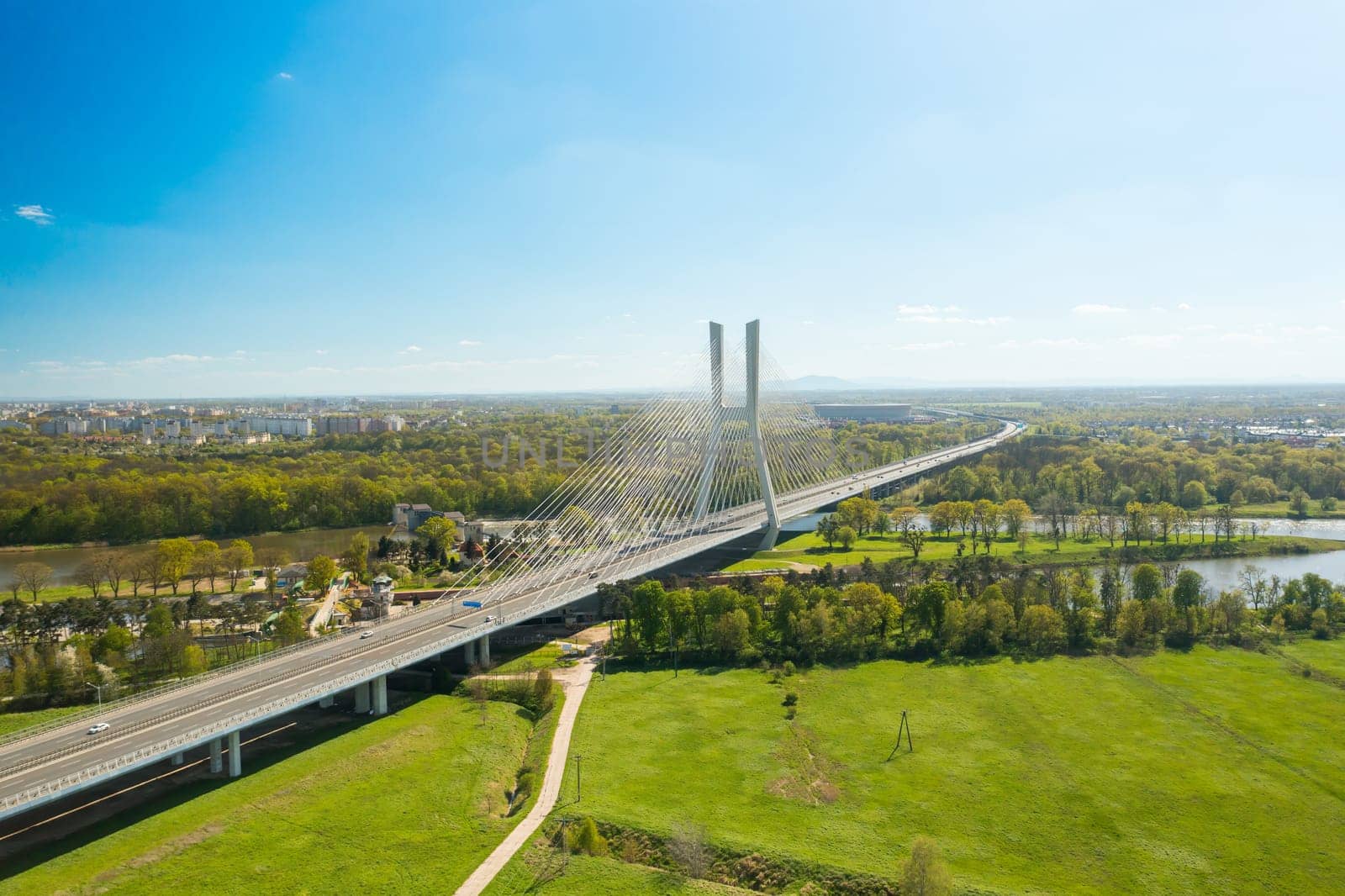 Famous cable-stayed Redzinski Bridge over blue flowing river among lush green forests. Scenic nature and urban infrastructure near Wroclaw aerial view