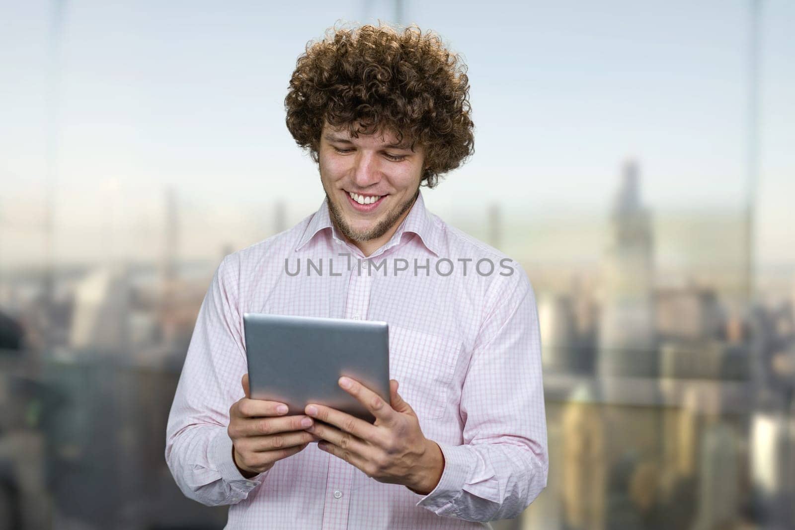 Excited young happy caucasian man holding a tablet pc device. Guy playing mobile videogame app or watching digital video stream holding cell phone indoors.