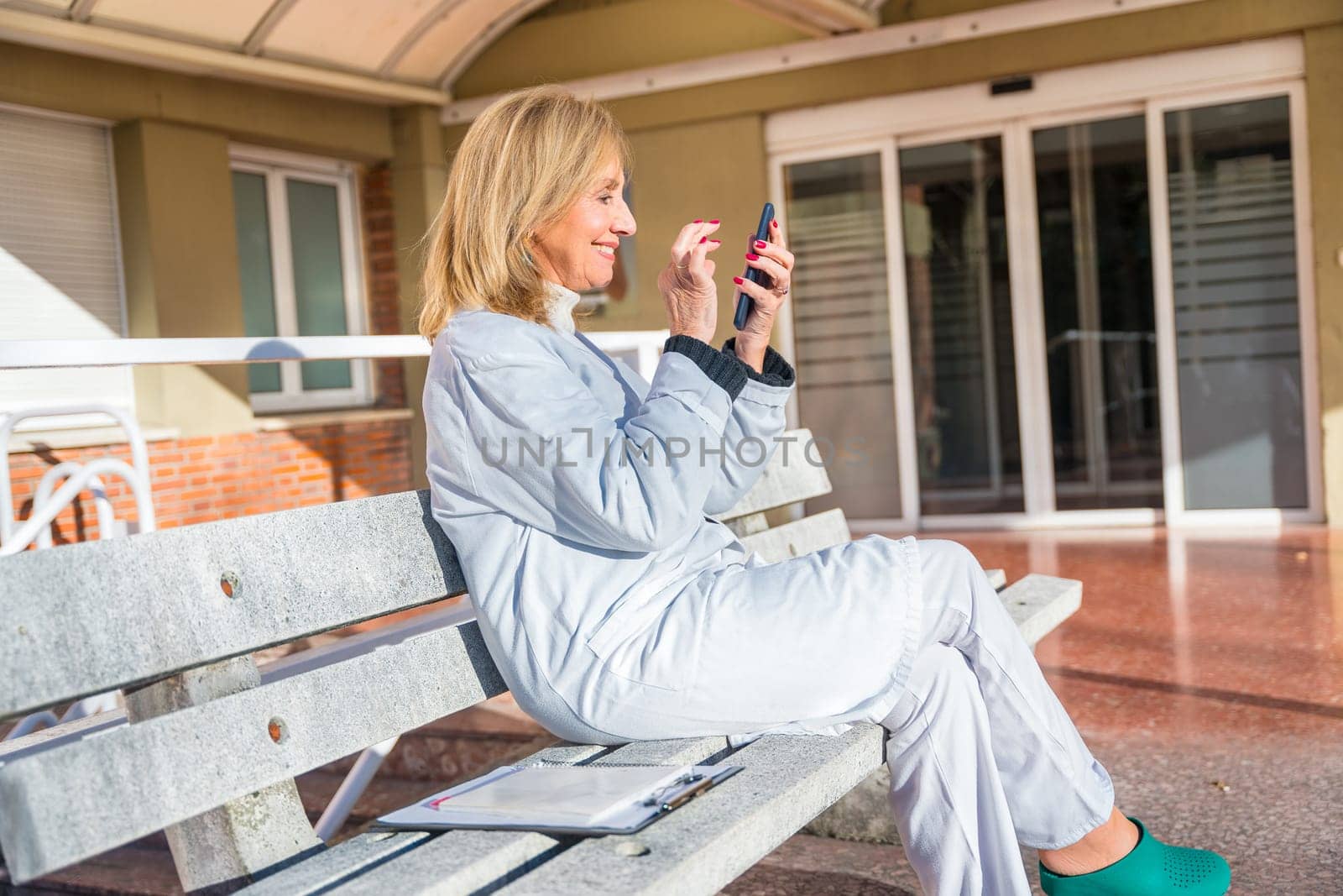 Side view of a mature female doctor using mobile during a work break outside the hospital