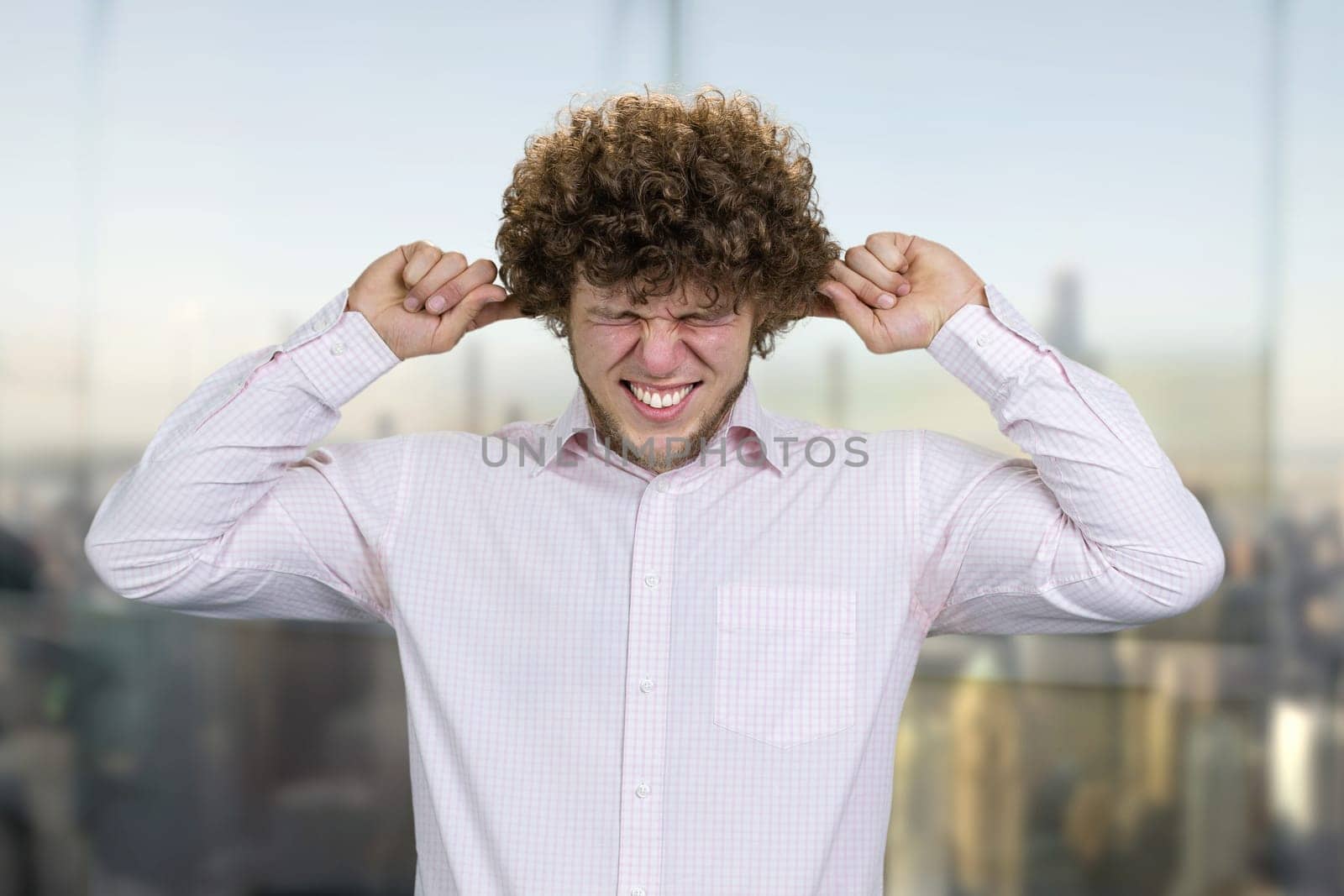 Caucasian young man in white shirt close his ears with both fingers. He doesn't want to hear that. Nervous breakdown concept. Blurred cityscape in the background.