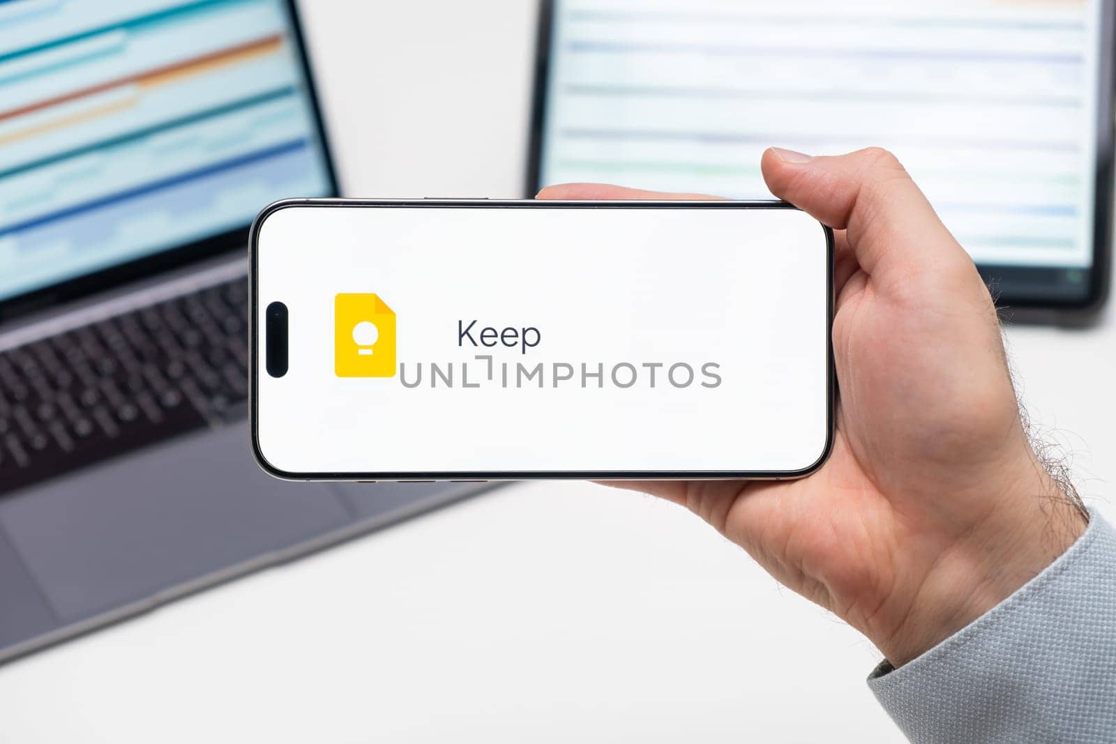 Keep logo of app on the screen of mobile phone held by man in front of the laptop and tablet, December 2023, Prague, Czech Republic