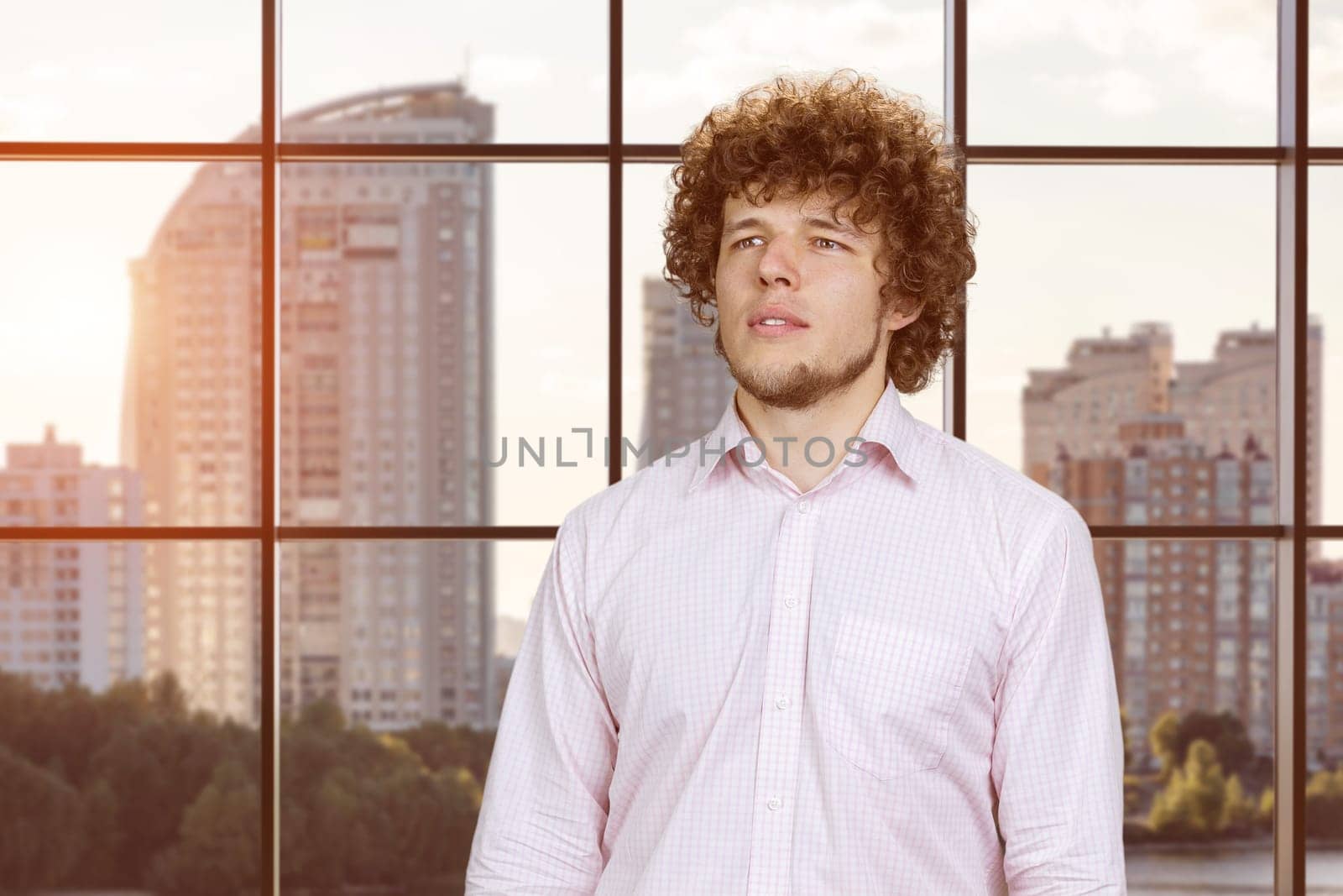 Portrait of a happy young attractive man with curly hair. Checkered indoor window in the background.