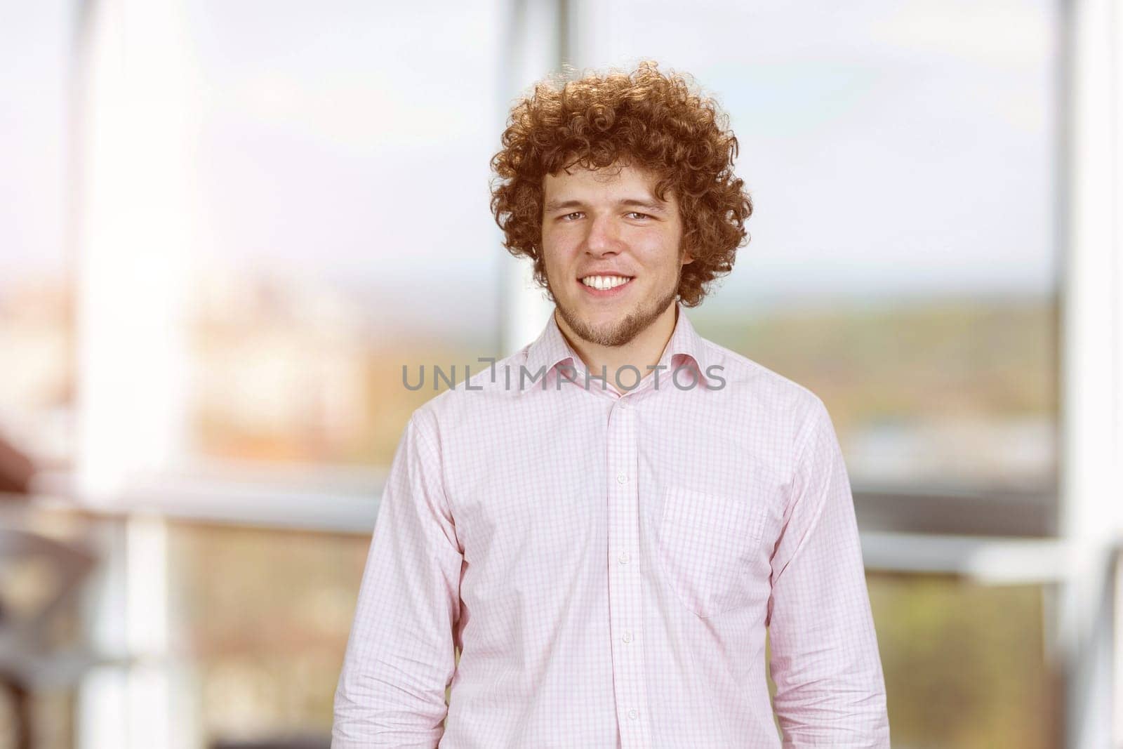 Portrait of a happy young cheerful man with curly hair. Indoor window in the background.