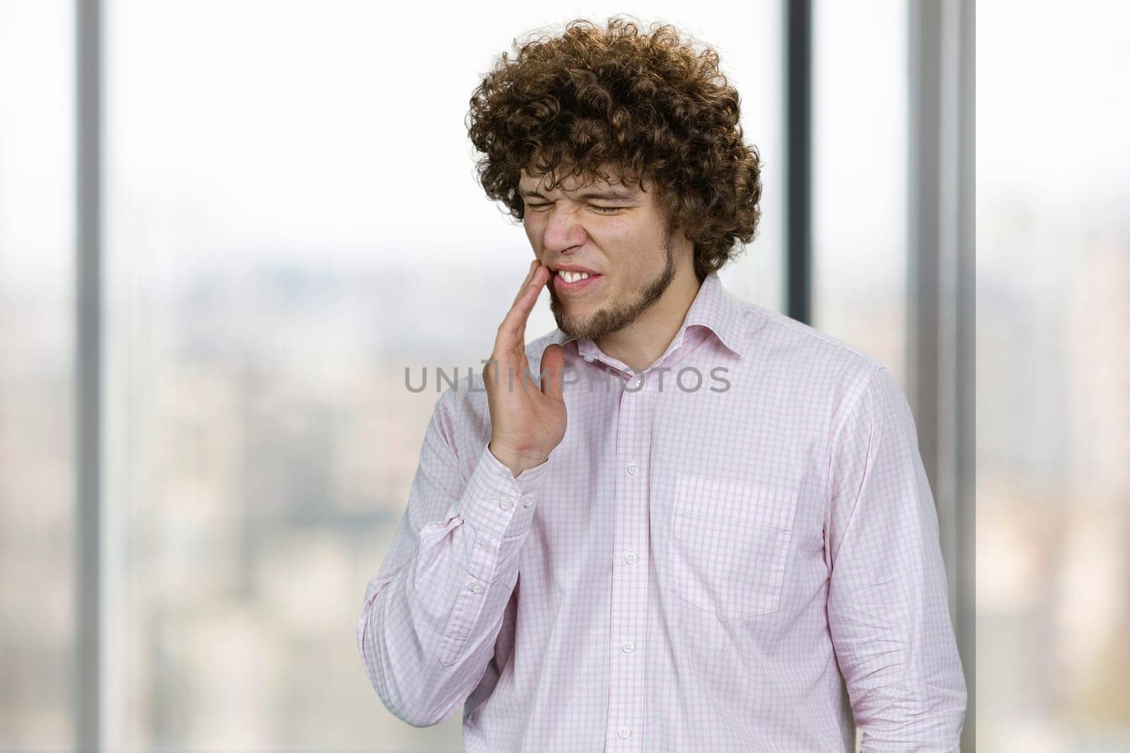 Handsome caucasian man touching cheek with hand. Painful expression because of toothache or dental illness on teeth.