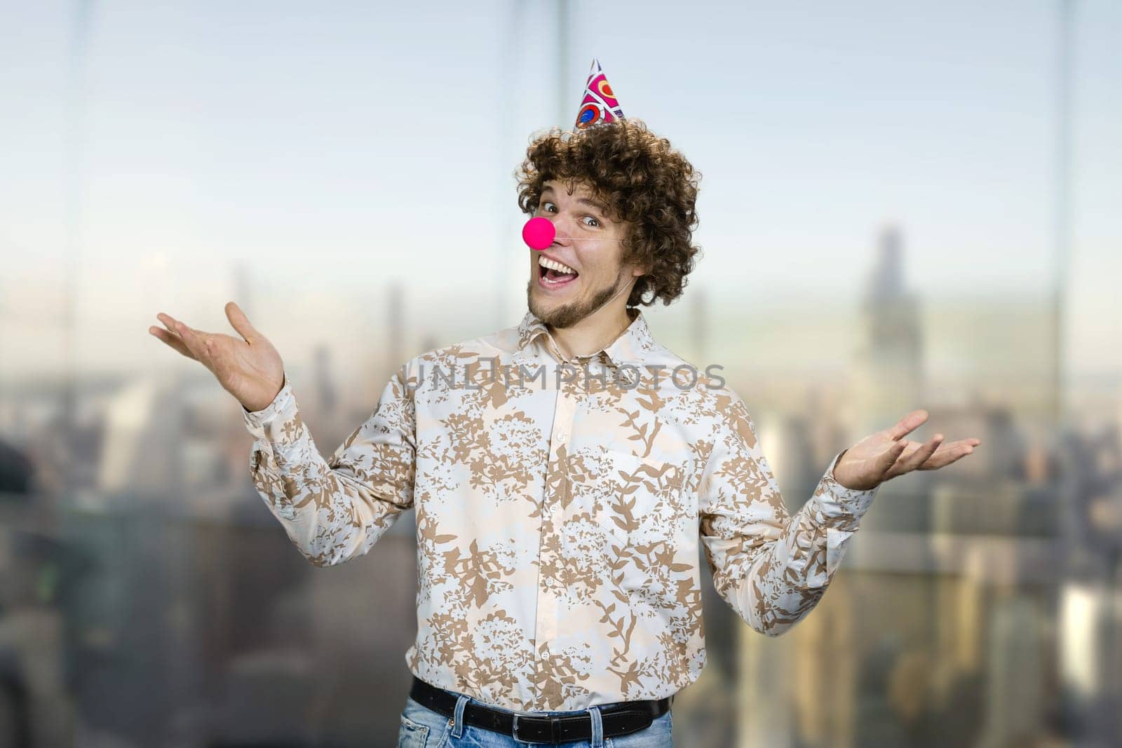 Portrait of a young caucasian guy with curly hair wearing a clowns nose. Happy birthday concept.