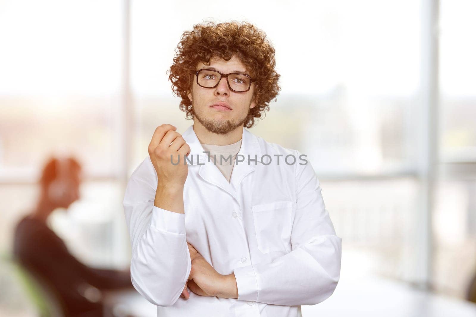 Portrait of a smart thoughtful young man with curly hair wearing glasses. Office setting in the background.