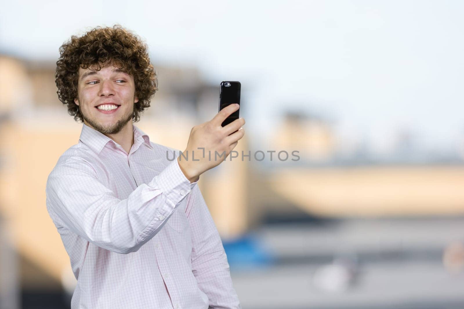 Portrait of a happy smiling young man with curly hair making a selfie. Blurred indoor background.