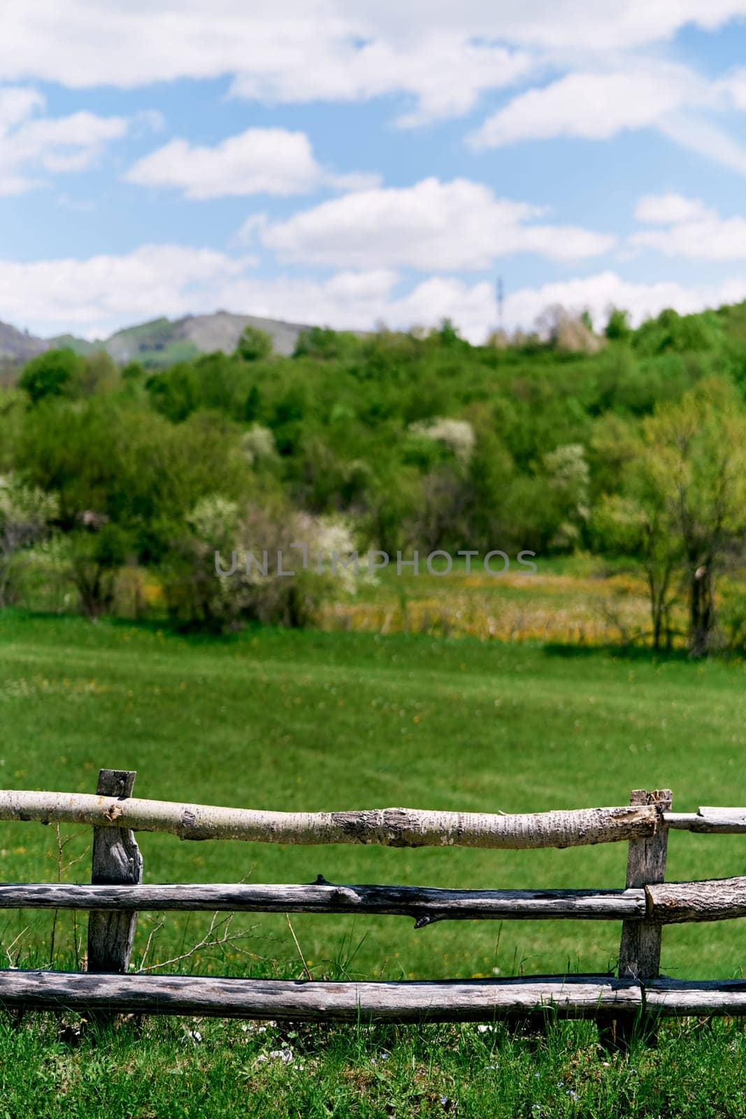 Wooden fence on a green field with mountains in the background by Nadtochiy