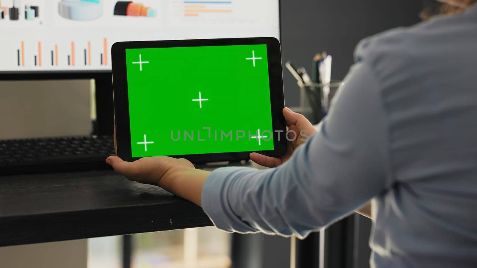 Worker examines greenscreen on tablet in agency coworking space office, looking at chromakey screen with isolated copyspace on mobile gadget. Employee holding chromakey device.