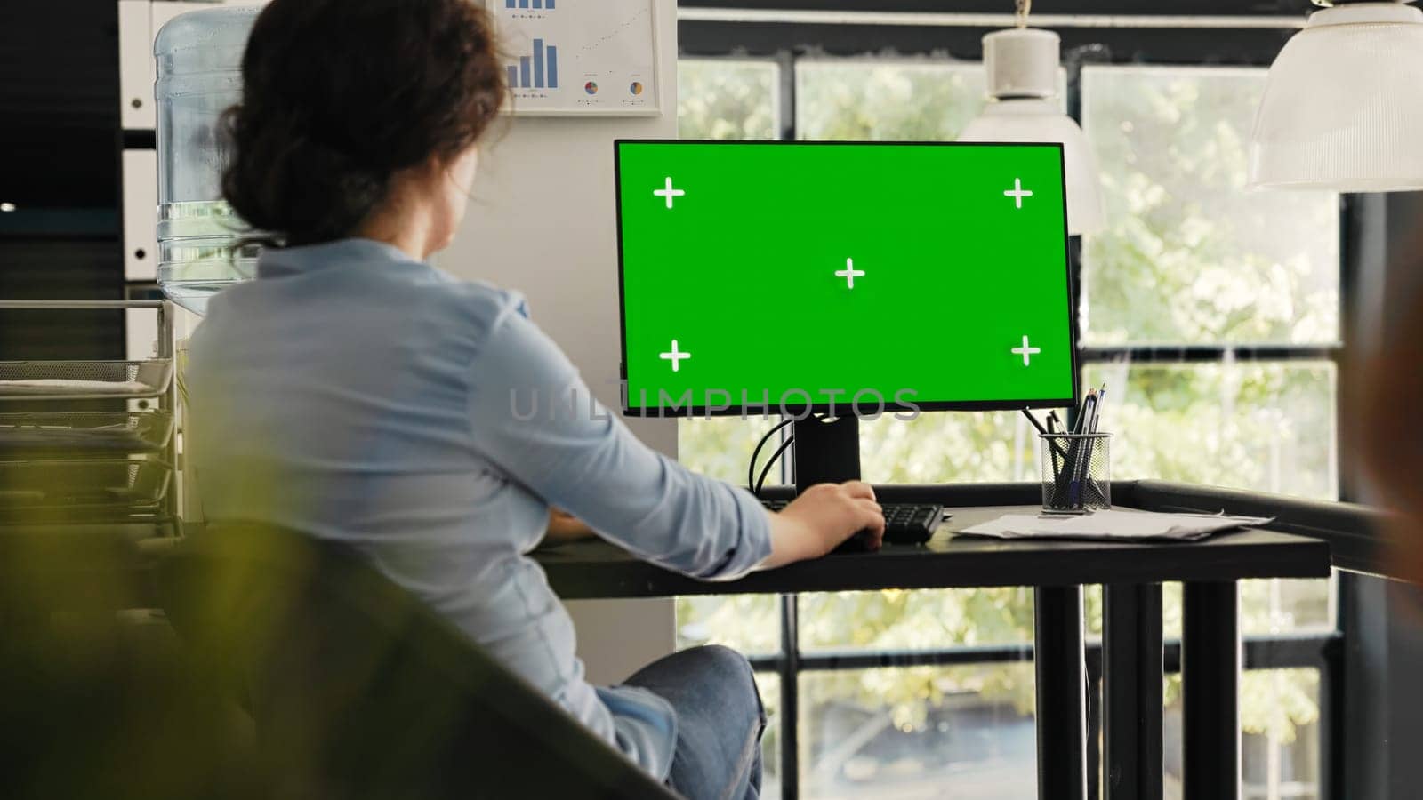 Specialist watches greenscreen desktop sitting at office desk, checking blank chromakey display on monitor. Woman typing information and looking at isolated mockup layout on computer.