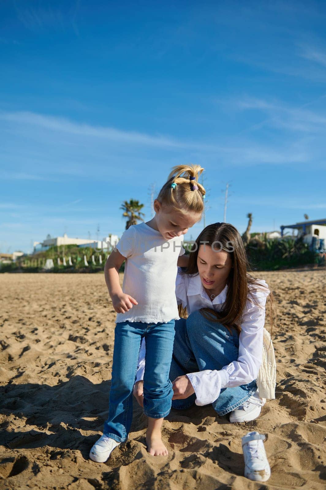 Happy mother and daughter playing together on the beach, building castles from the sand, enjoying nice time outdoor. People. Family relationships. Lifestyle. Maternity and childhood concept
