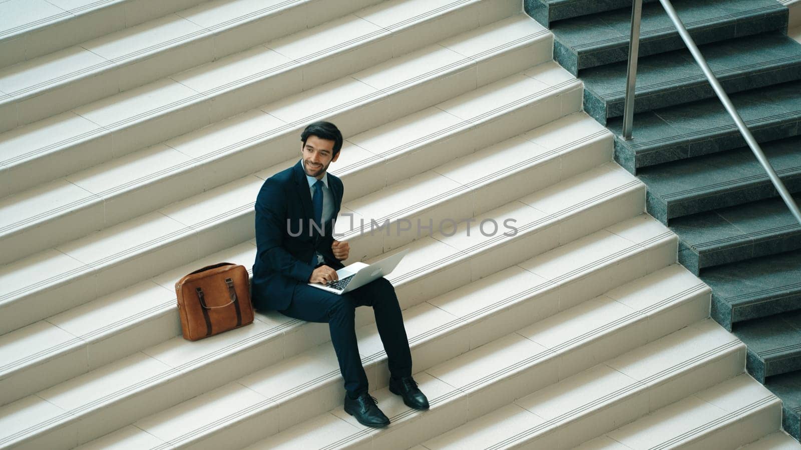 Top view of investor working or planing strategy by using laptop at stair. Professional business man wearing suit while working and typing data analysis by using laptop at modern hotel. Exultant.