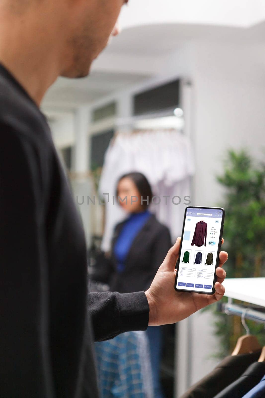Clothing store customer male hand grasping smartphone and checking apparel on boutique website. Caucasian client using mobile device for browsing clothing items in a shopping mall.