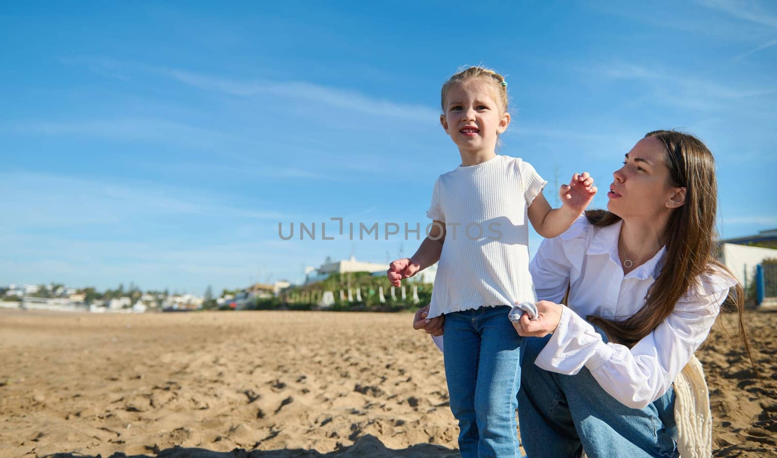 Authentic happy young Caucasian woman, loving mother and her cute little child girl enjoying happy time together on the beach on warm sunny day. People. Family. Lifestyle. Maternity and childhood