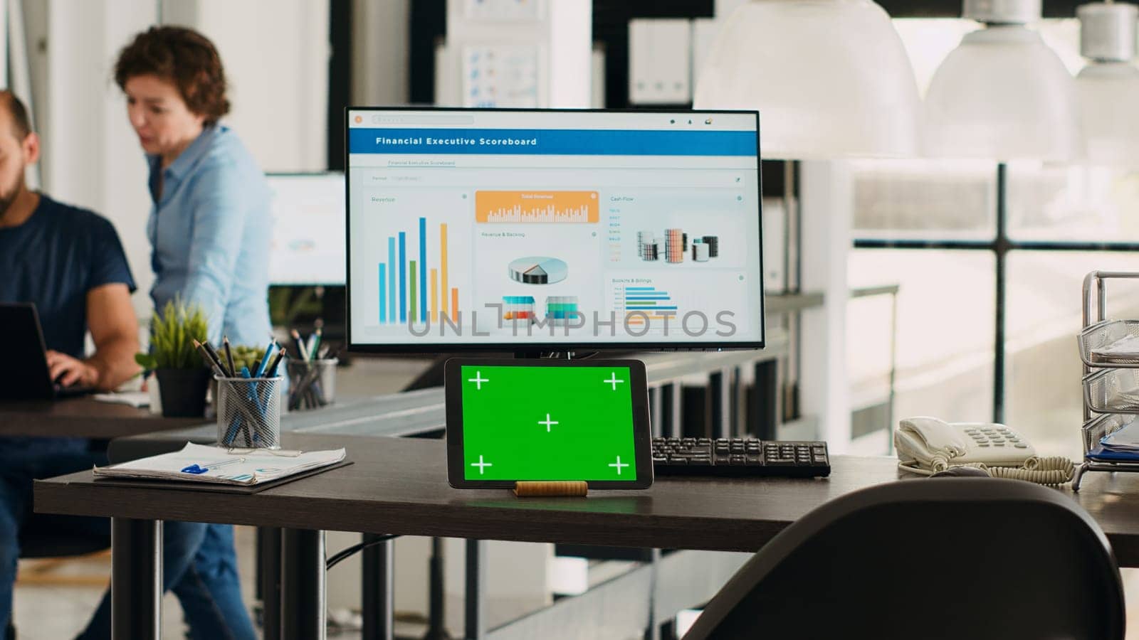 Desk with tablet showing greenscreen, empty workstation in creative agency coworking space. Modern gadget running isolated chromakey display in small business workplace, mockup screen.