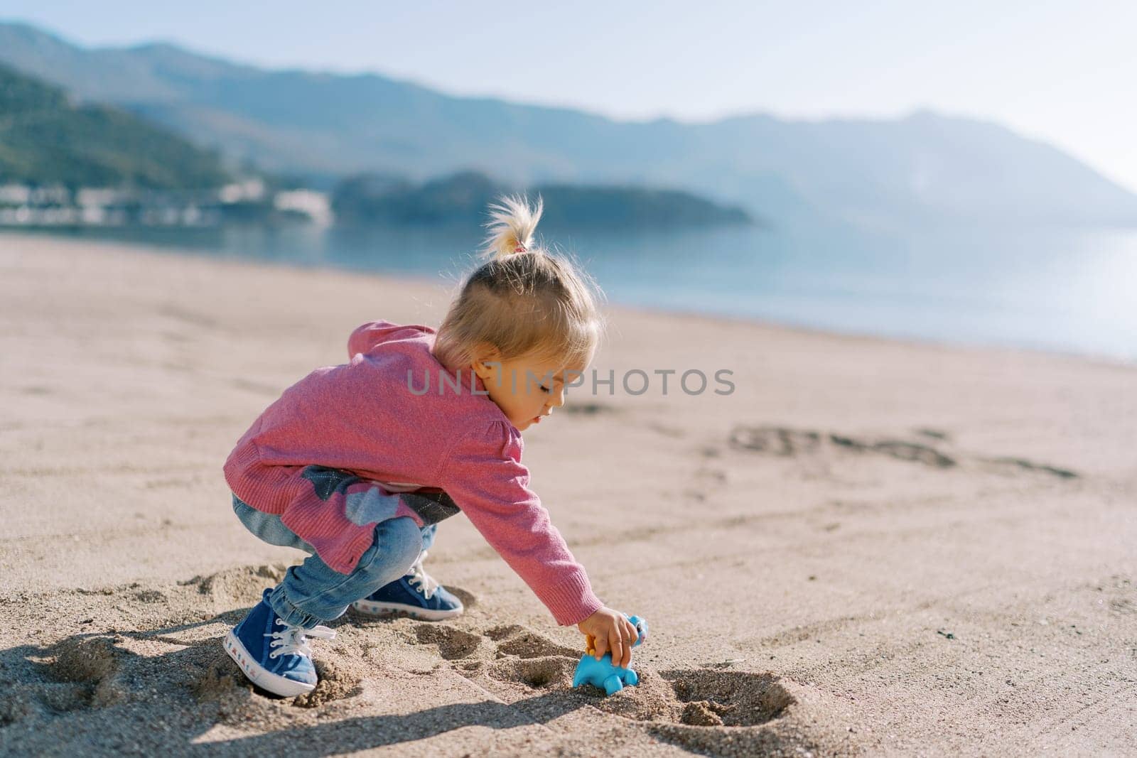 Little girl plays on the sand on the beach with a toy plastic dinosaur. High quality photo