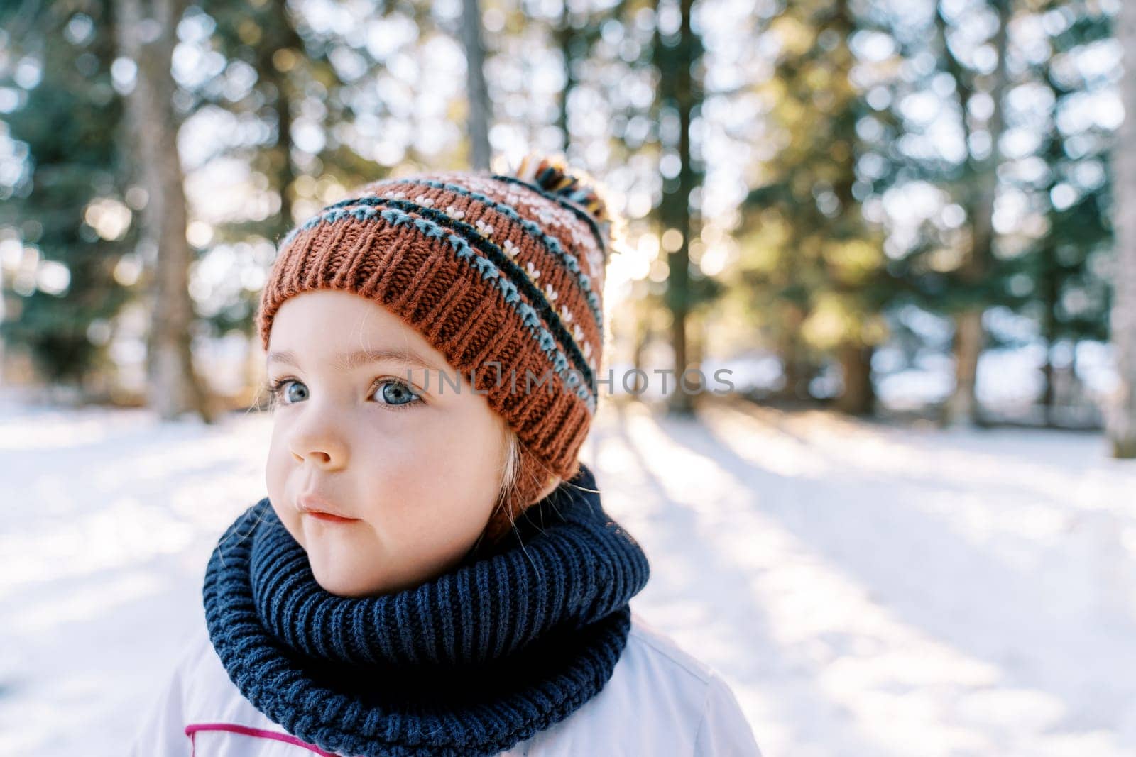 Little thoughtful girl stands in a snowy forest and looks away. High quality photo