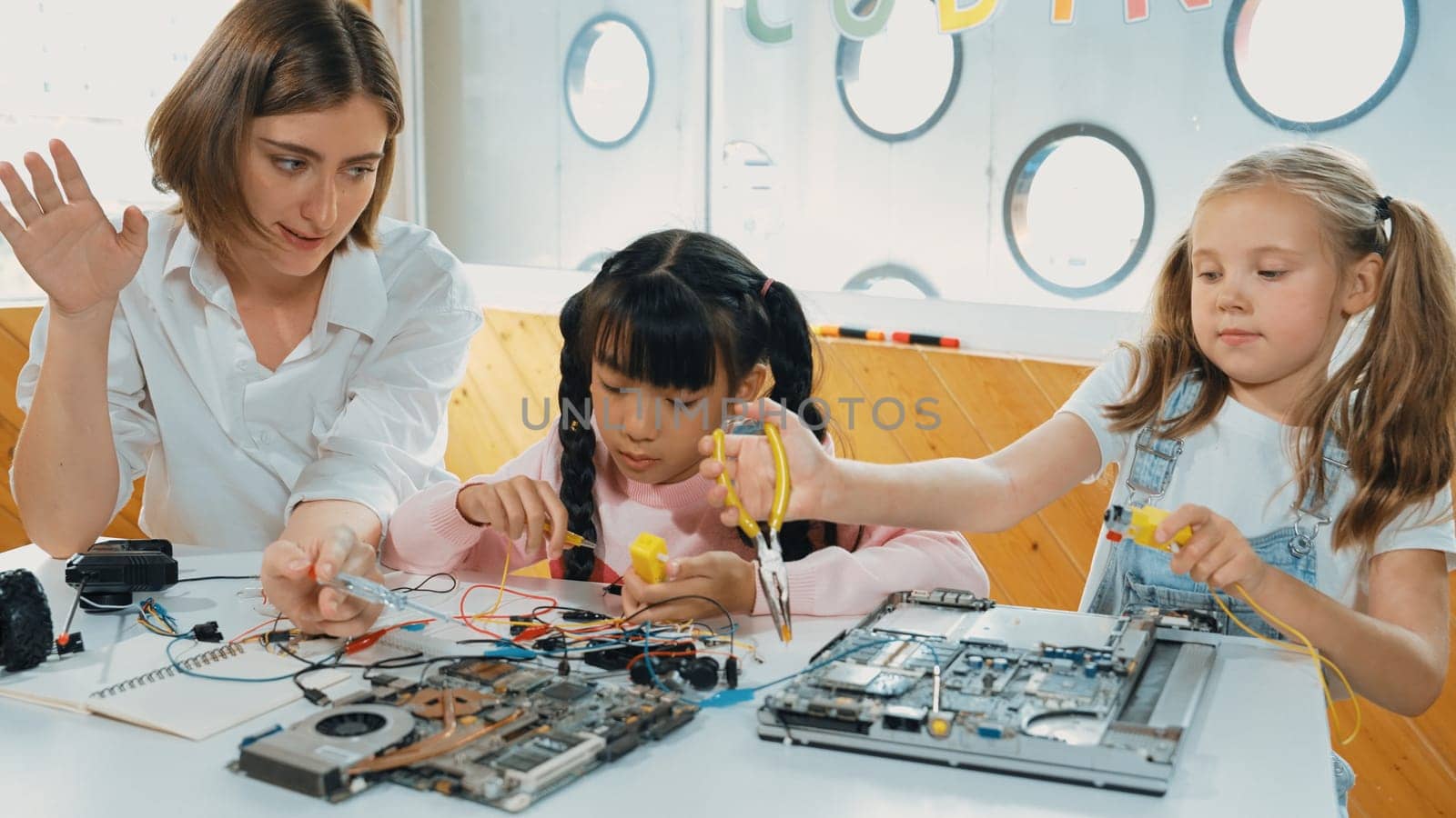 Skilled caucasian teacher teach and explain students about digital electrical tool. Expert girl learn electronic equipment and use to fix motherboard at table with chips and wires placed. Erudition.