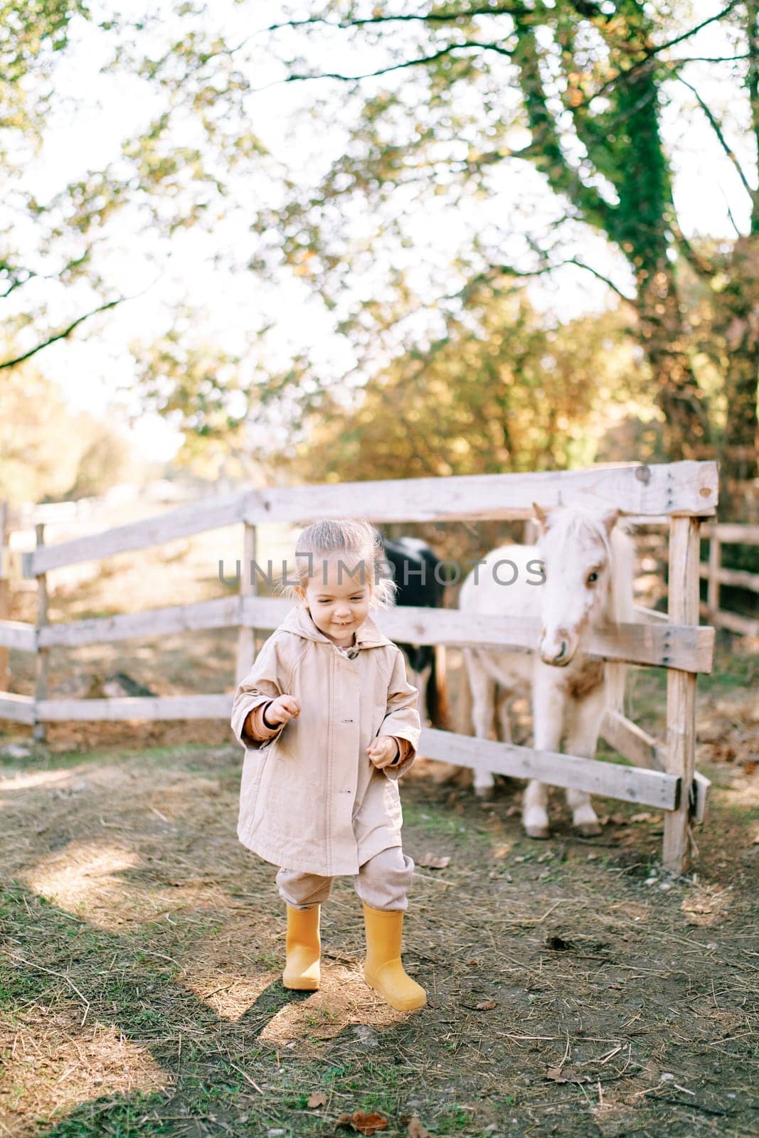 Little smiling girl walks along the path from the pony in the paddock. High quality photo