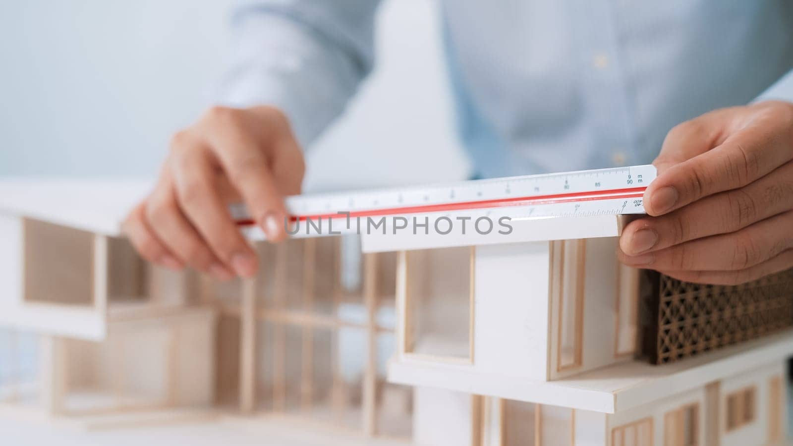 Closeup image of professional male architect engineer hand uses ruler to measure house model at modern office. Creative living and design concept. Blurring background. Focus on hand. Immaculate
