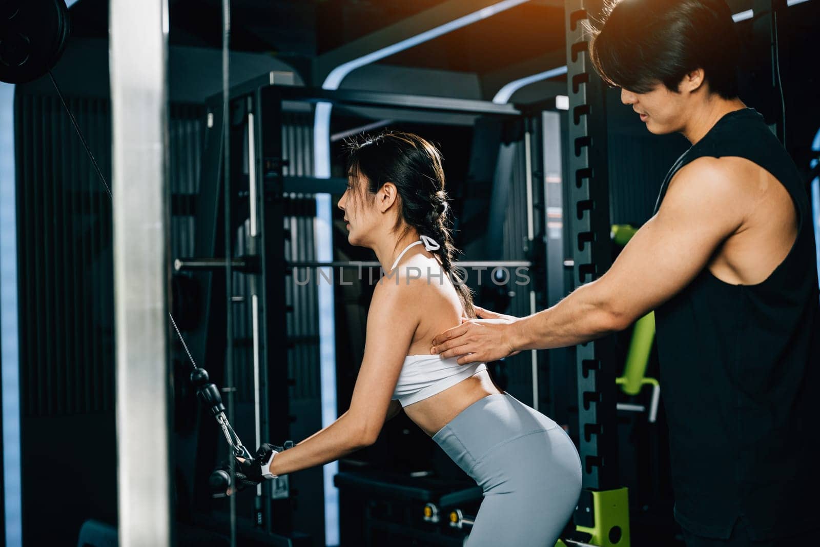 Male fitness coach teaching a woman how to use a pulldown cable machine by Sorapop