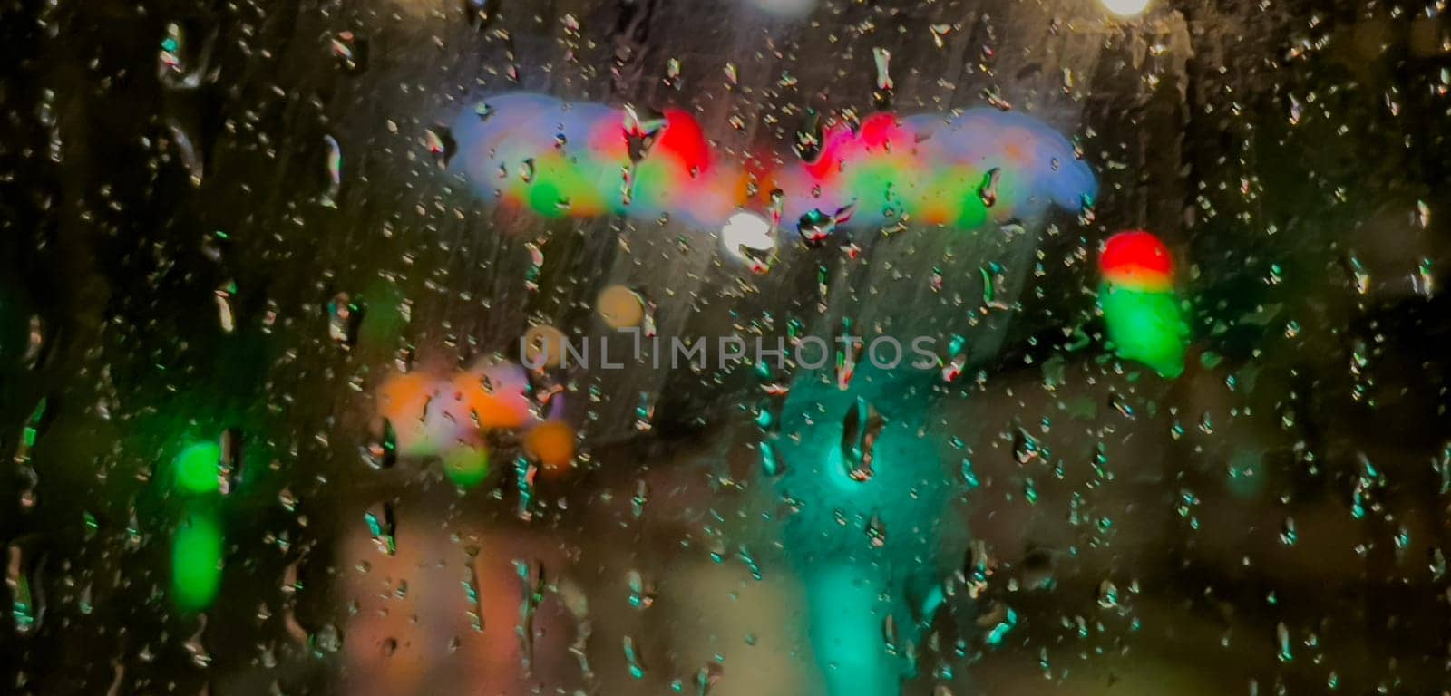 Rain bokeh road lights. Abstract shot of evening city traffic bokeh. Multicolored lights of the evening city and passing cars through a wet rainy window