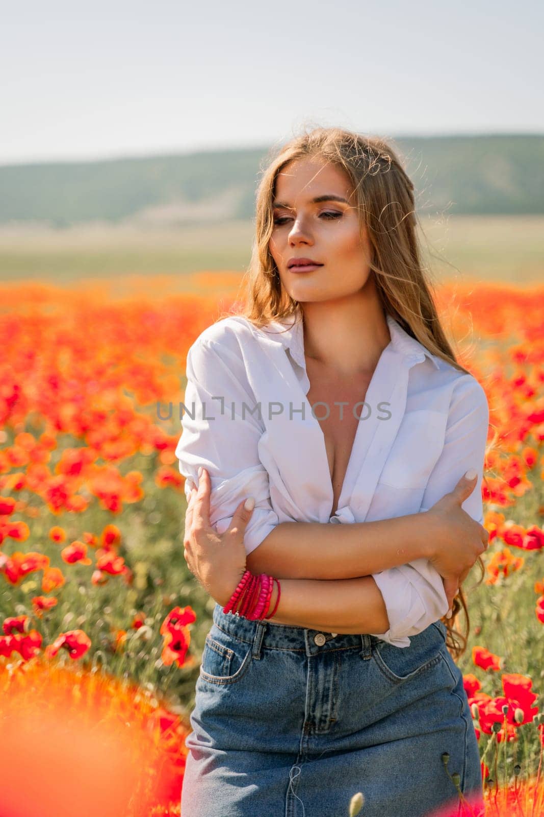 Happy woman in a poppy field in a white shirt and denim skirt with a wreath of poppies on her head posing and enjoying the poppy field. by Matiunina