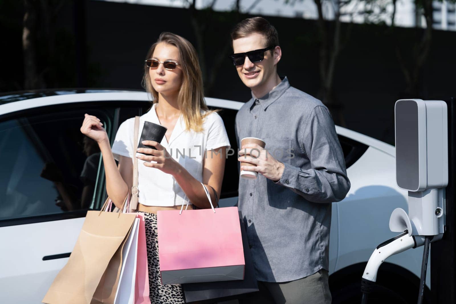 Young couple travel with EV electric car in green sustainable city innards by biancoblue