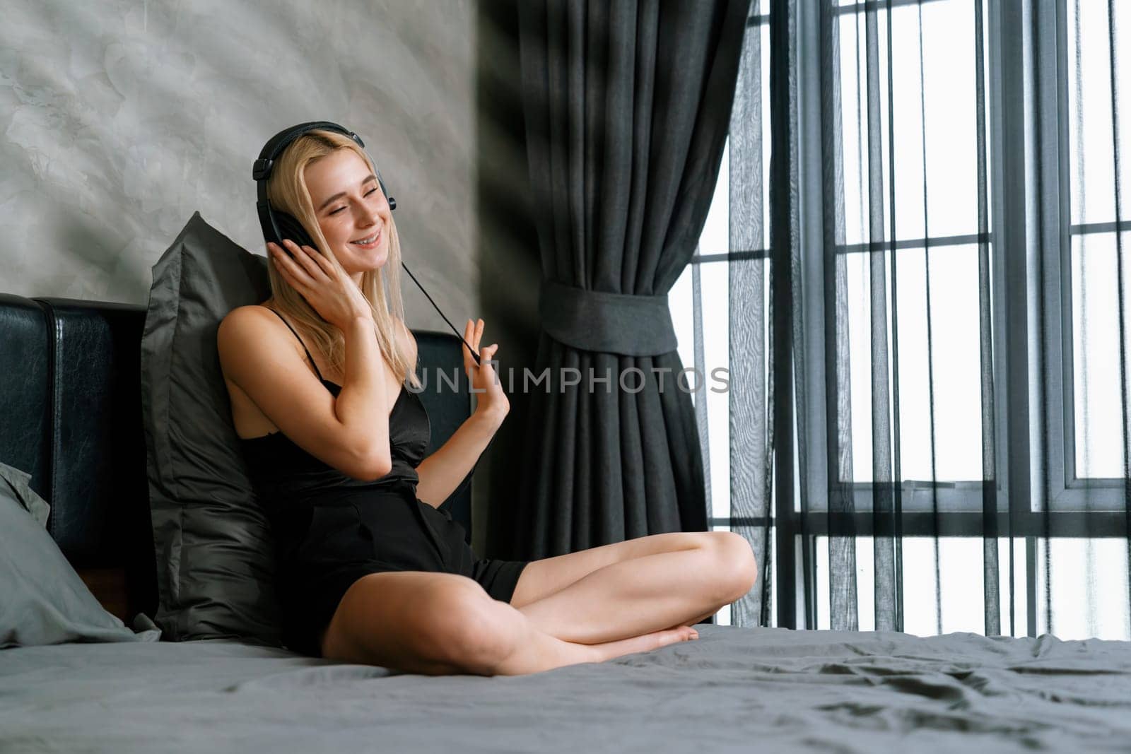 Young woman listening to music on headphone on her bed. Blithe by biancoblue