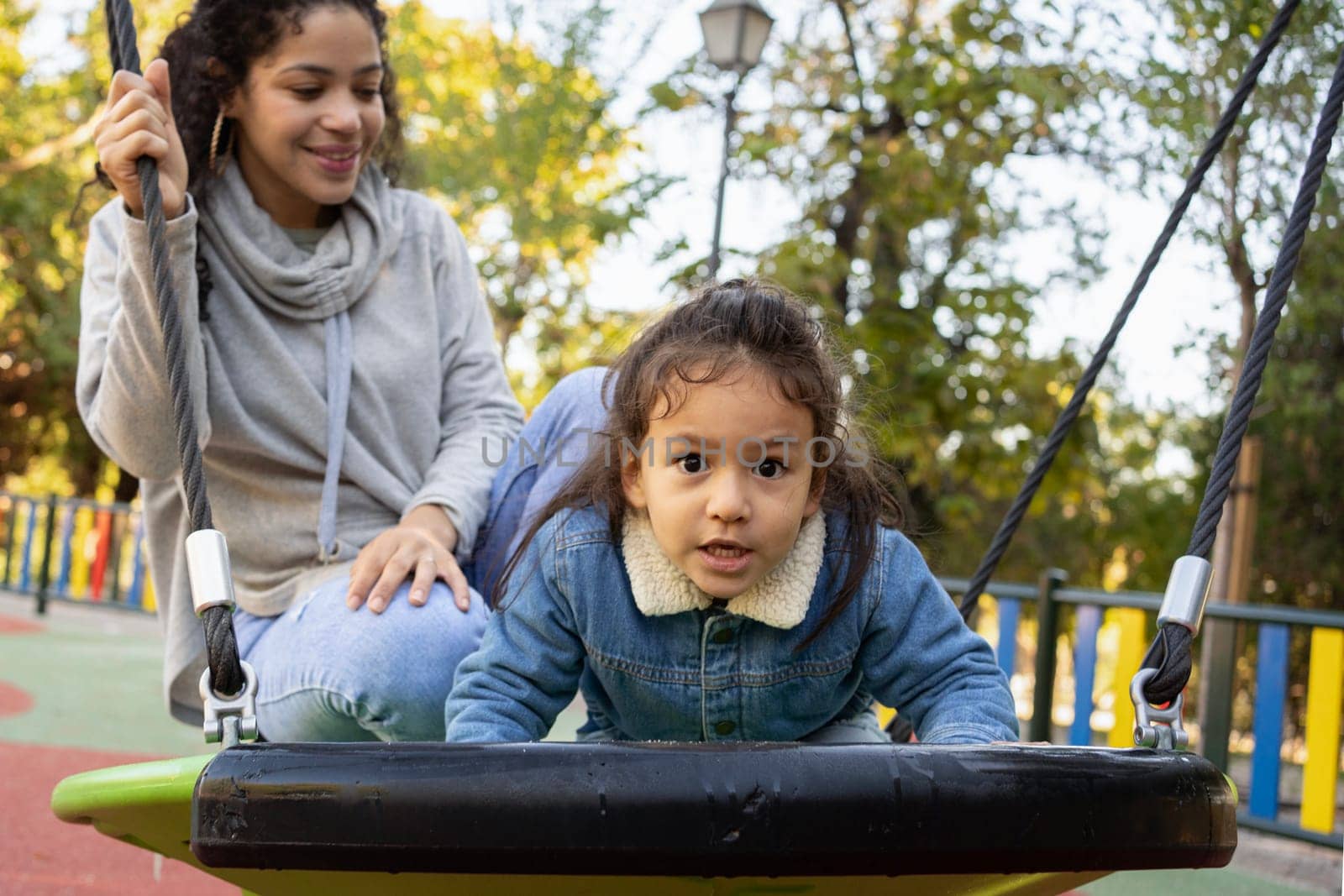 Portrait of happy little kid having fun with her mother at playground while looking at camera by papatonic