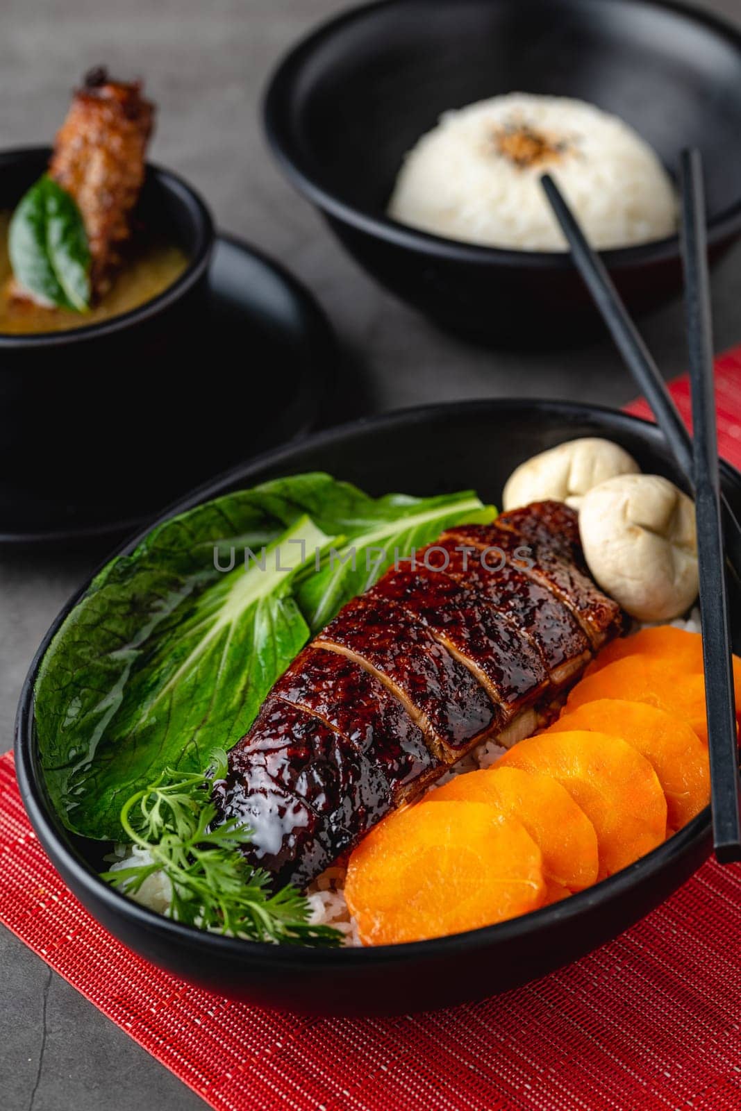 Roast duck with rice and teriyaki sauce on black plate by Sonat