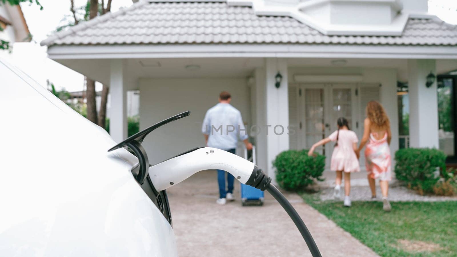 Happy family return from holiday and travel while recharging electric EV car's battery at home charging station. EV car and modern family concept. Synchronos