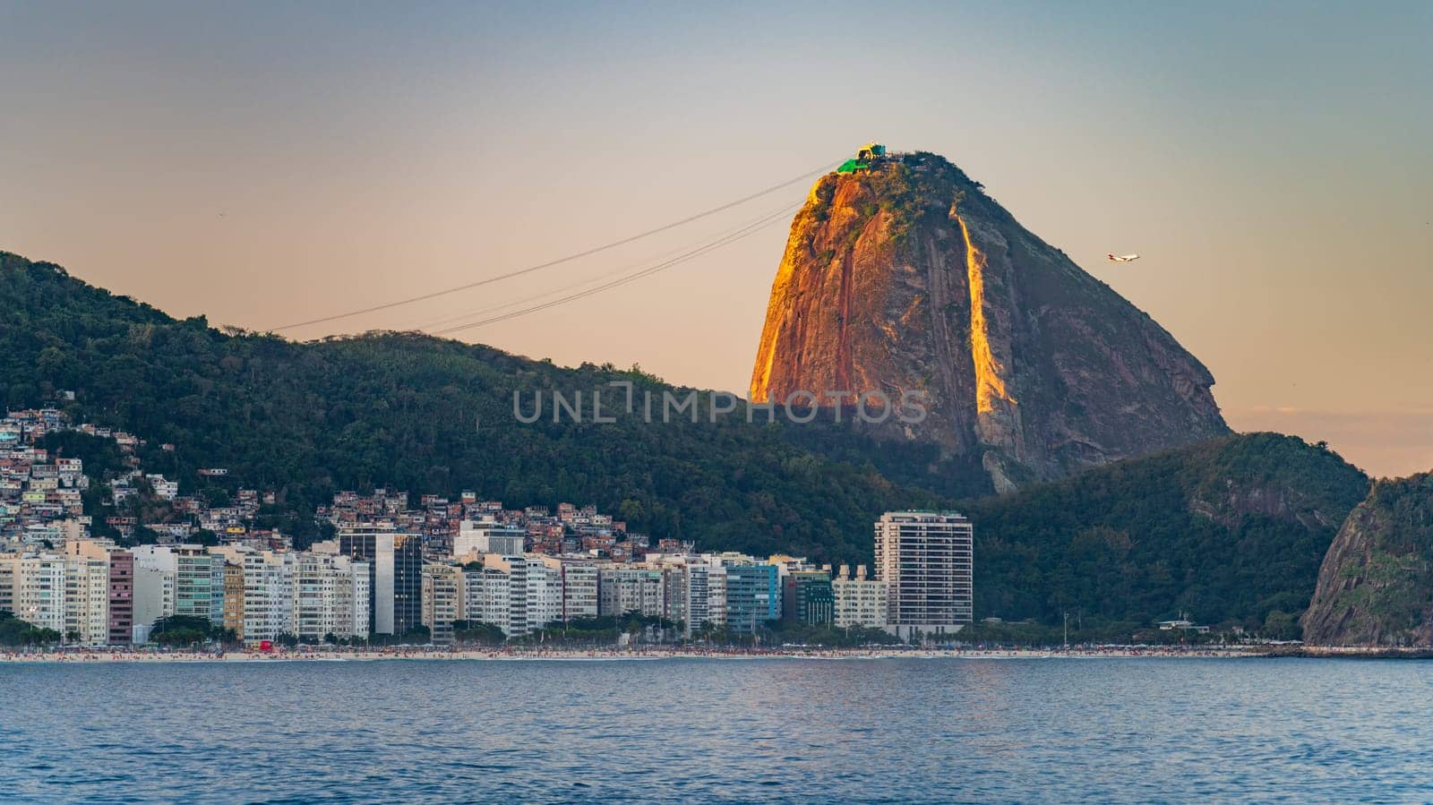 Sunset illuminates Sugarloaf Mountain against Rio cityscape.