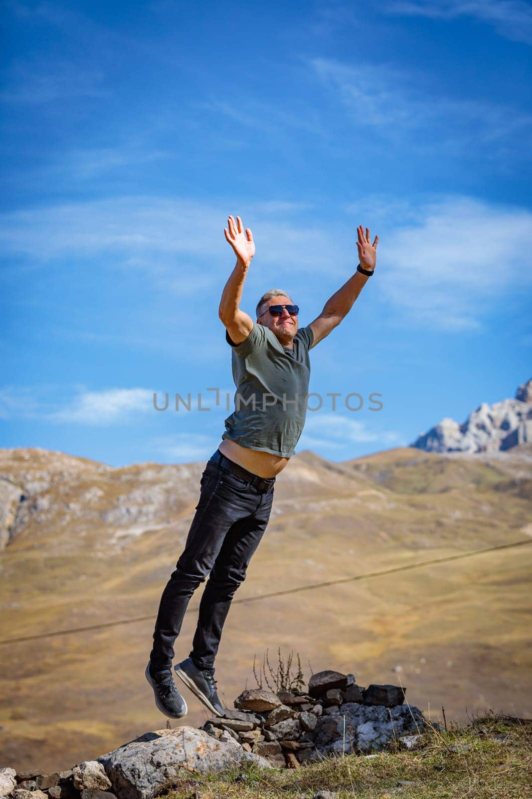 A man happily jumps on the top of a mountain, exhilarating the mesmerizing scenery and his achievement by Yurich32