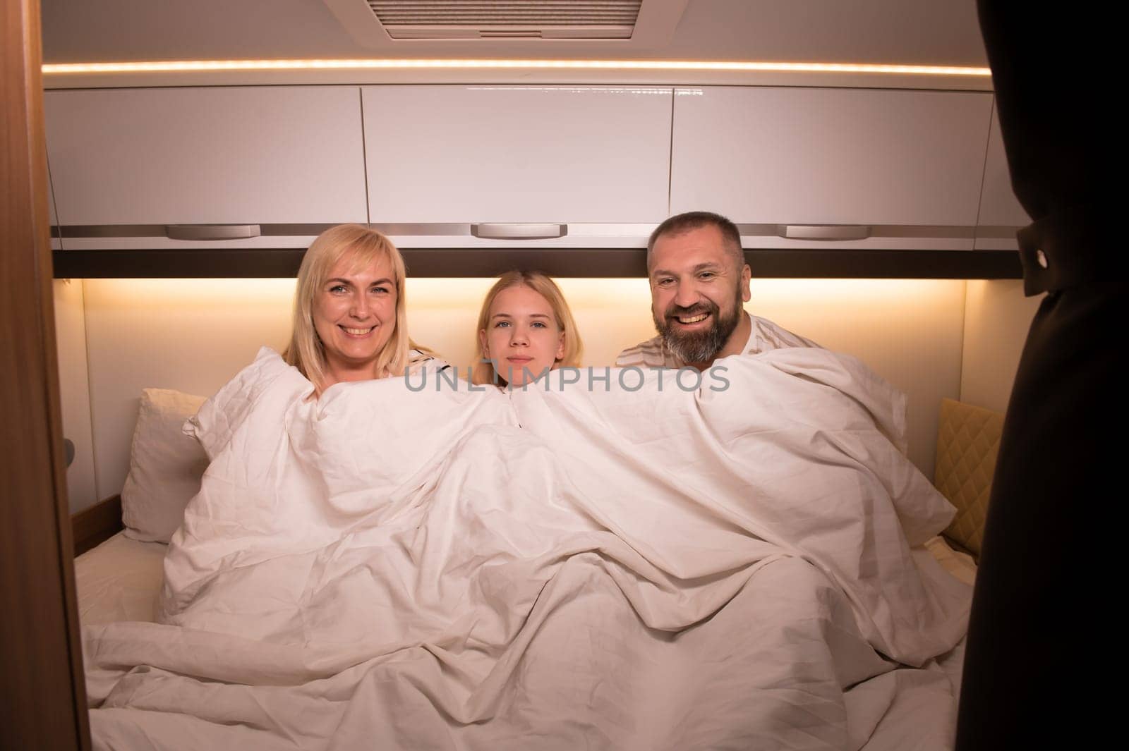 The family is getting ready for bed sitting on the bed in their motorhome.