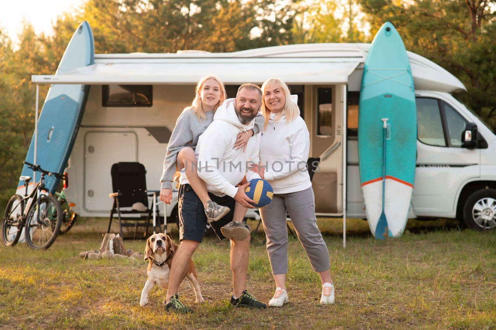 Happy parents with their child playing with a ball near their mobile home in the woods by Lobachad