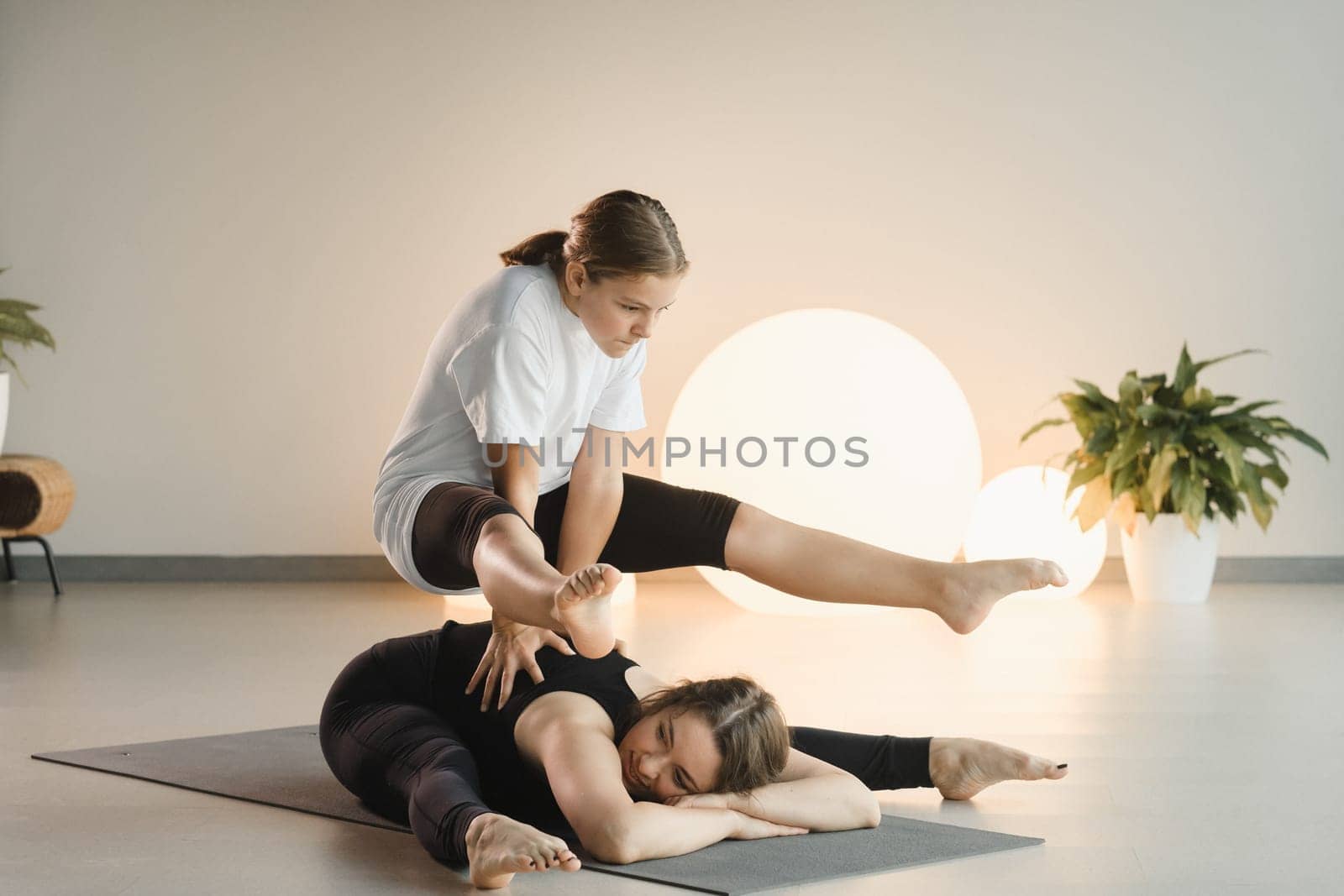 Mom and teenage daughter do gymnastics together in the fitness room. A woman and a girl train in the gym.