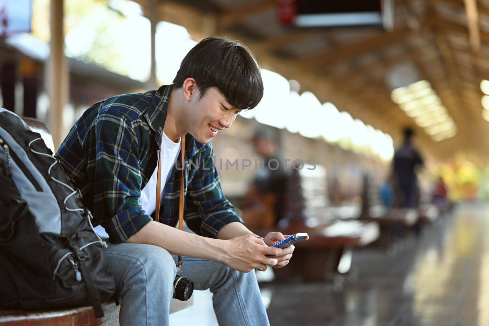 Handsome man backpacker using mobile phone at railway platform. Travel and vacations concept by prathanchorruangsak