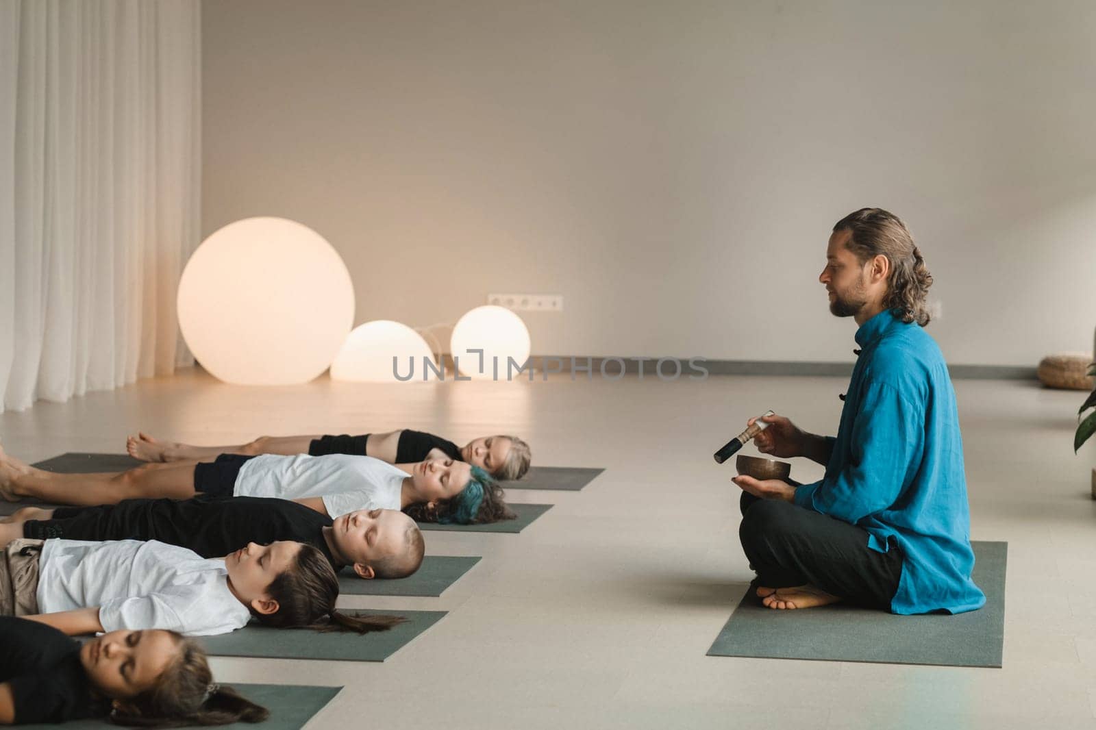 Children relax lying down to the sounds of a Tibetan bowl in the fitness room. Children's yoga.