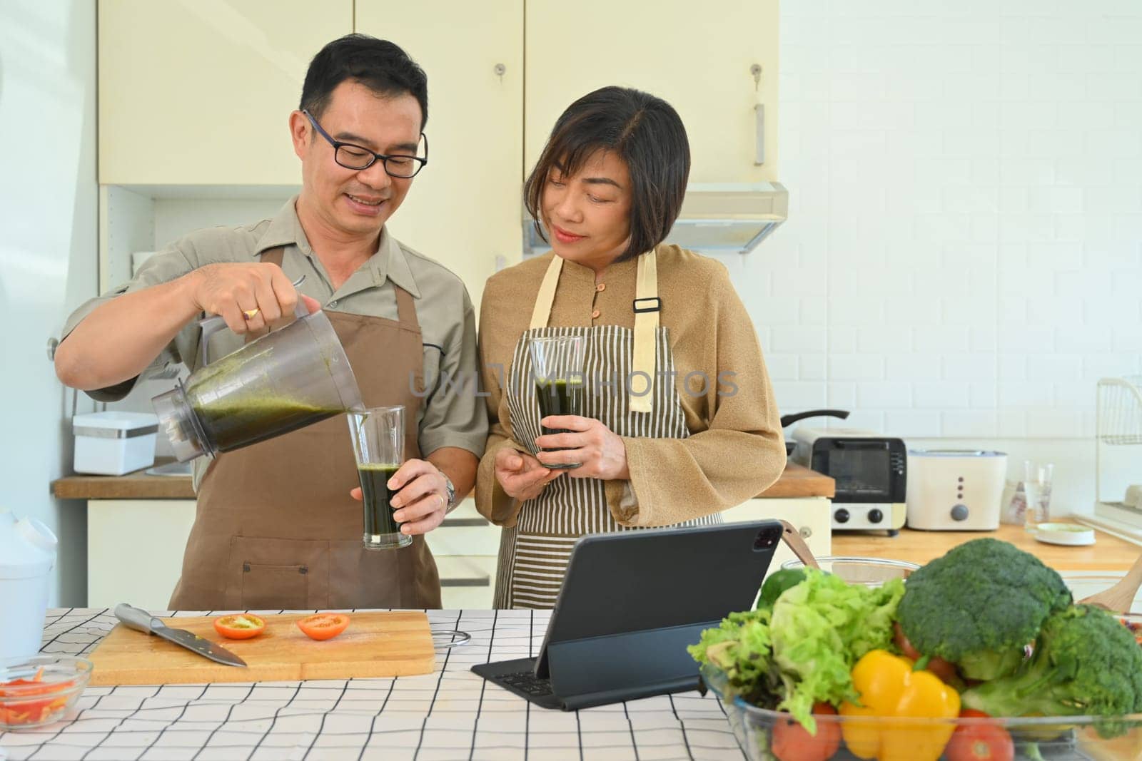 Happy middle age couple preparing vegan organic smoothie in kitchen. Healthy Lifestyle concept.