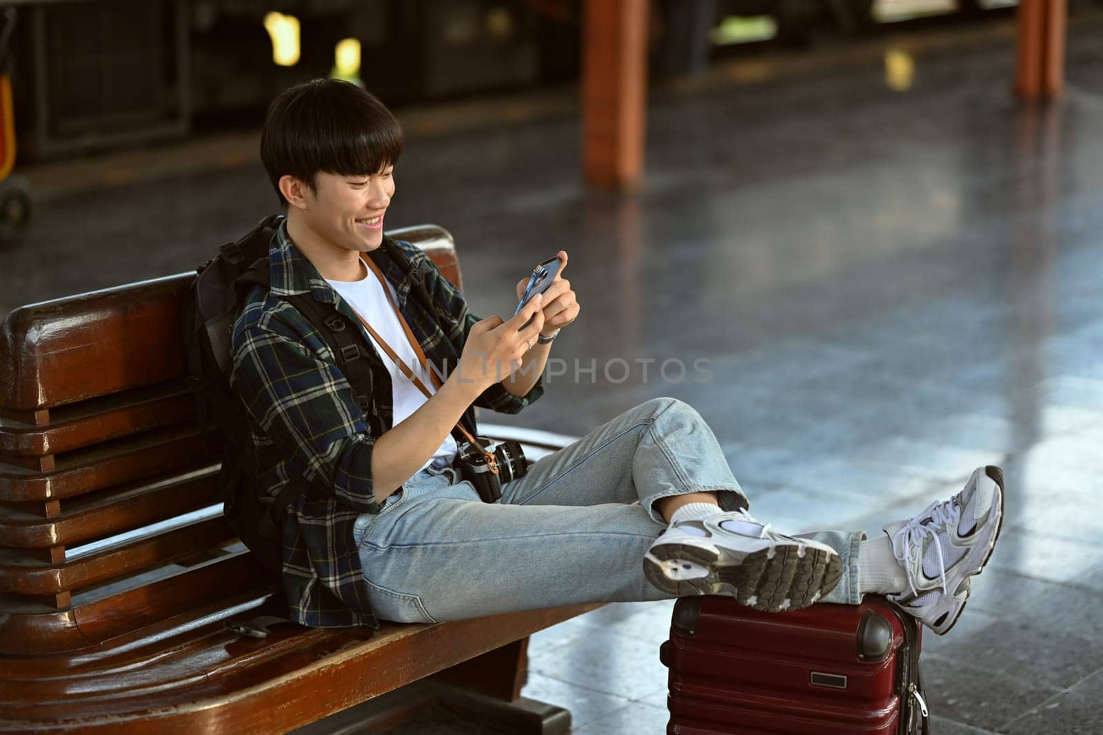 Happy Asian male traveler with suitcase using mobile phone while waiting train. Travel and vacations concept. by prathanchorruangsak