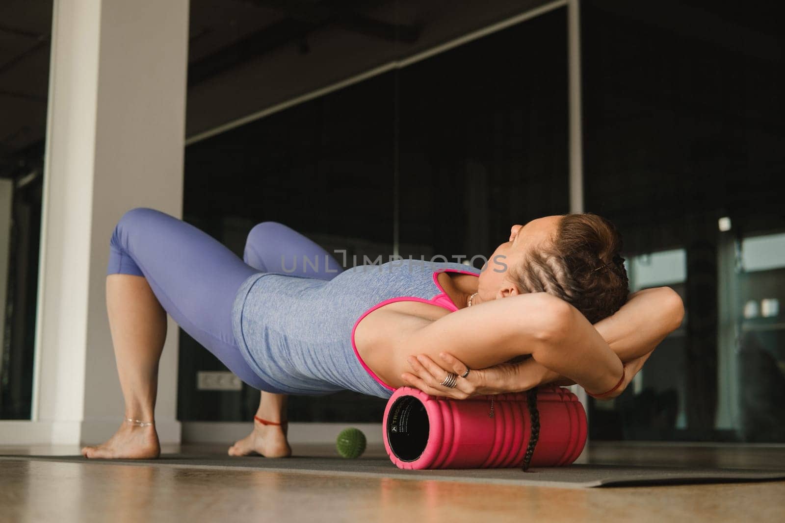 Slender girl doing yoga with a big massage roller on the floor.