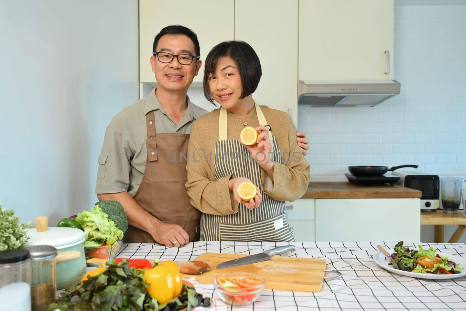 Happy retired couple in aprons cooking healthy food with organic ingredients in kitchen. Healthy lifestyle concept