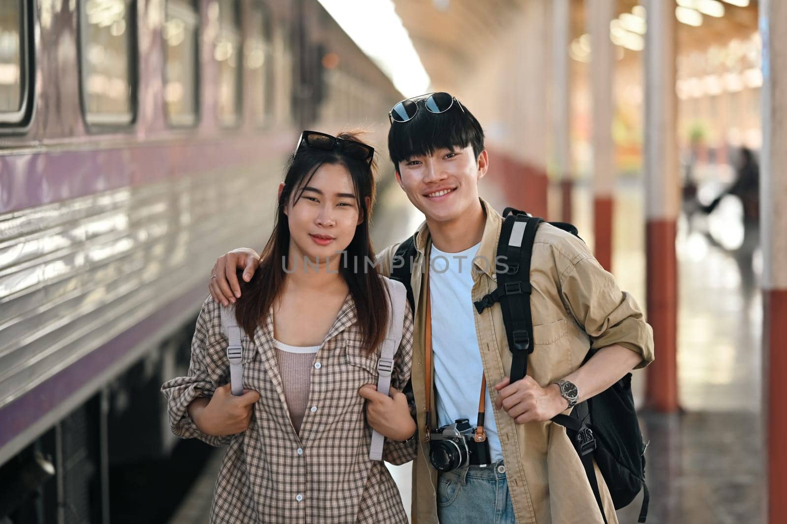 Beautiful young couple with backpack waiting for the train at railway station. Travel and vacations concept. by prathanchorruangsak